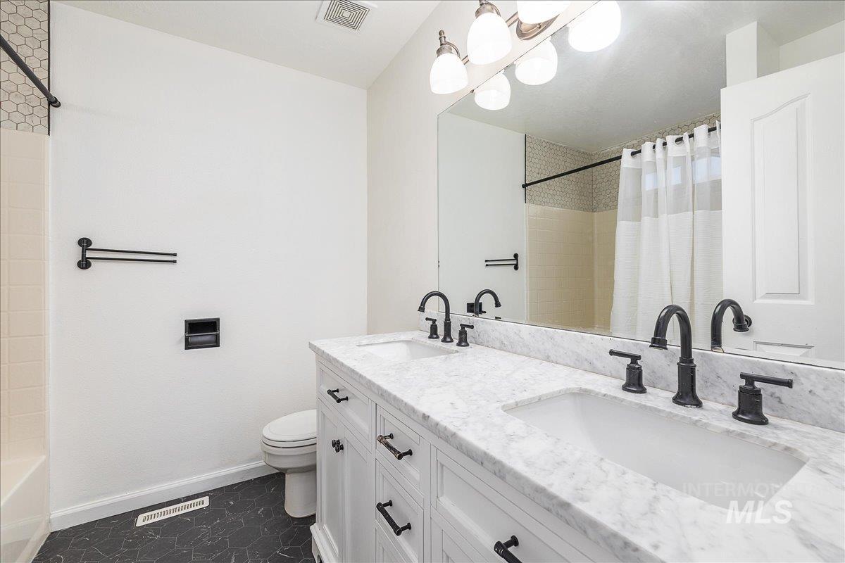 Bathroom featuring double vanity, dark tile patterned flooring, and shower / tub combo with curtain