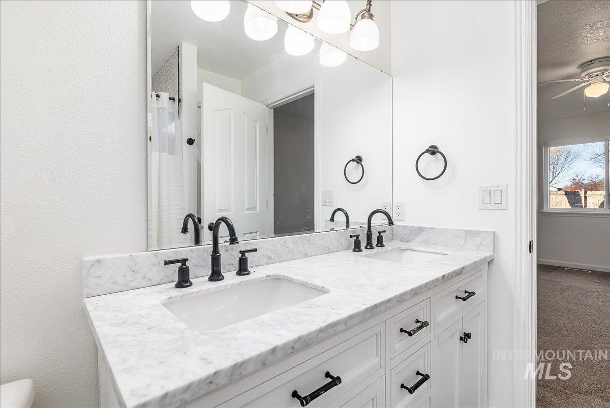 Full bath featuring curtained shower, double vanity, a ceiling fan, and dark carpet