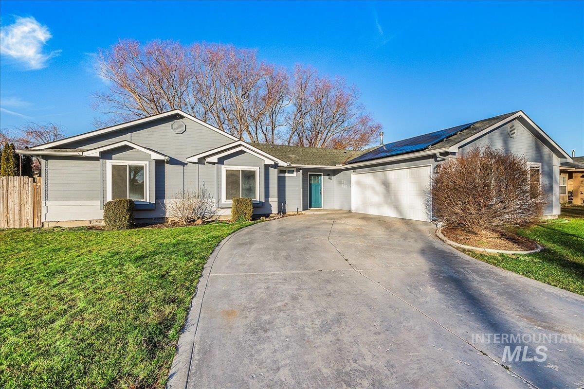 Single story home with an attached garage, concrete driveway, and roof mounted solar panels