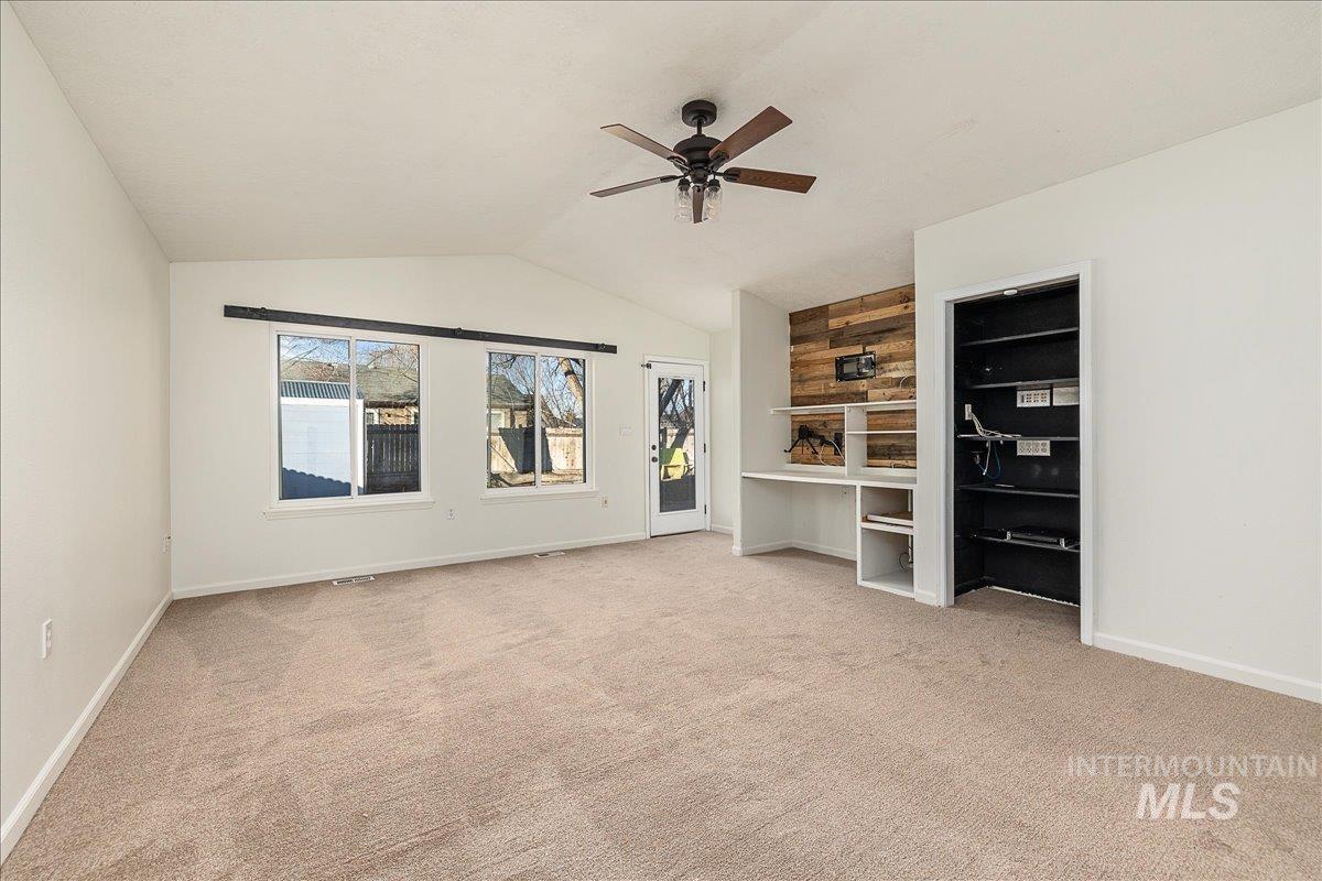 Unfurnished living room featuring light colored carpet, vaulted ceiling, and a ceiling fan