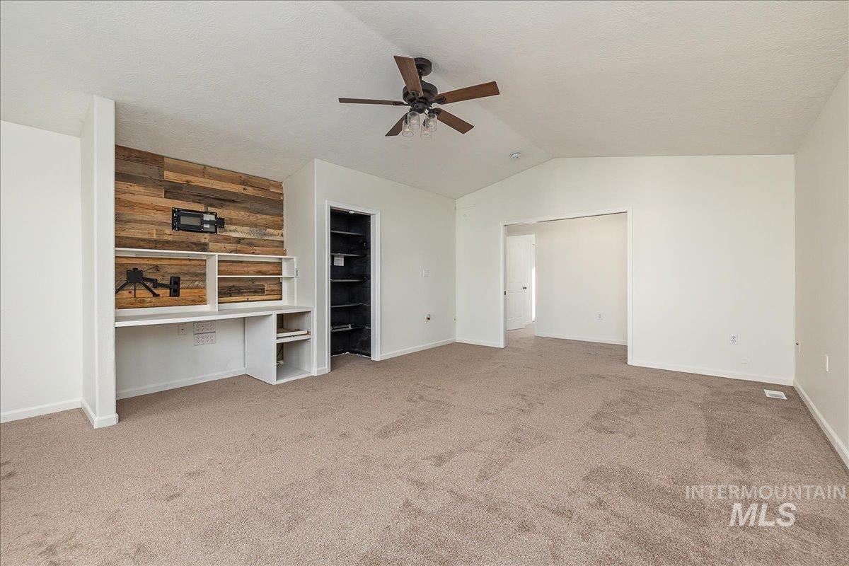 Unfurnished bedroom featuring lofted ceiling, light carpet, a ceiling fan, a textured ceiling, and wood walls
