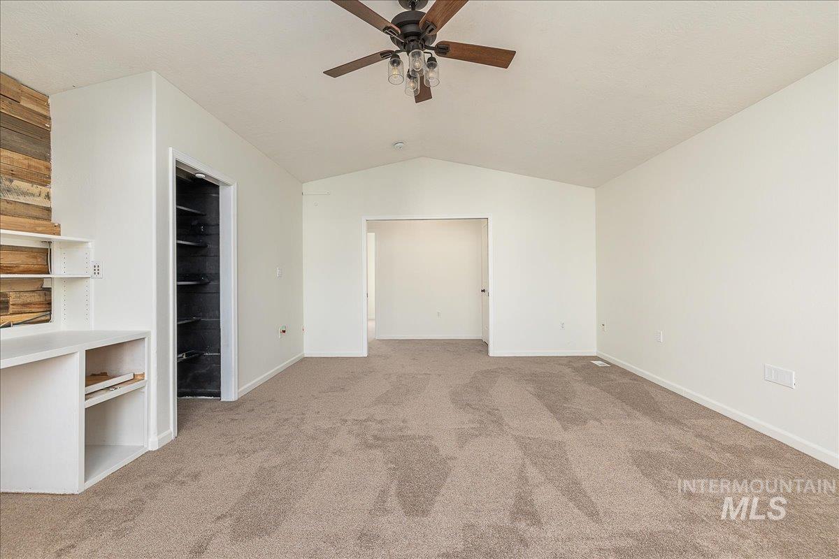 Unfurnished bedroom featuring a walk in closet, vaulted ceiling, carpet, and a ceiling fan