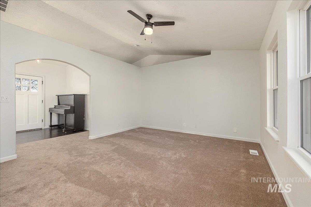 Unfurnished living room featuring vaulted ceiling, carpet flooring, a ceiling fan, and arched walkways