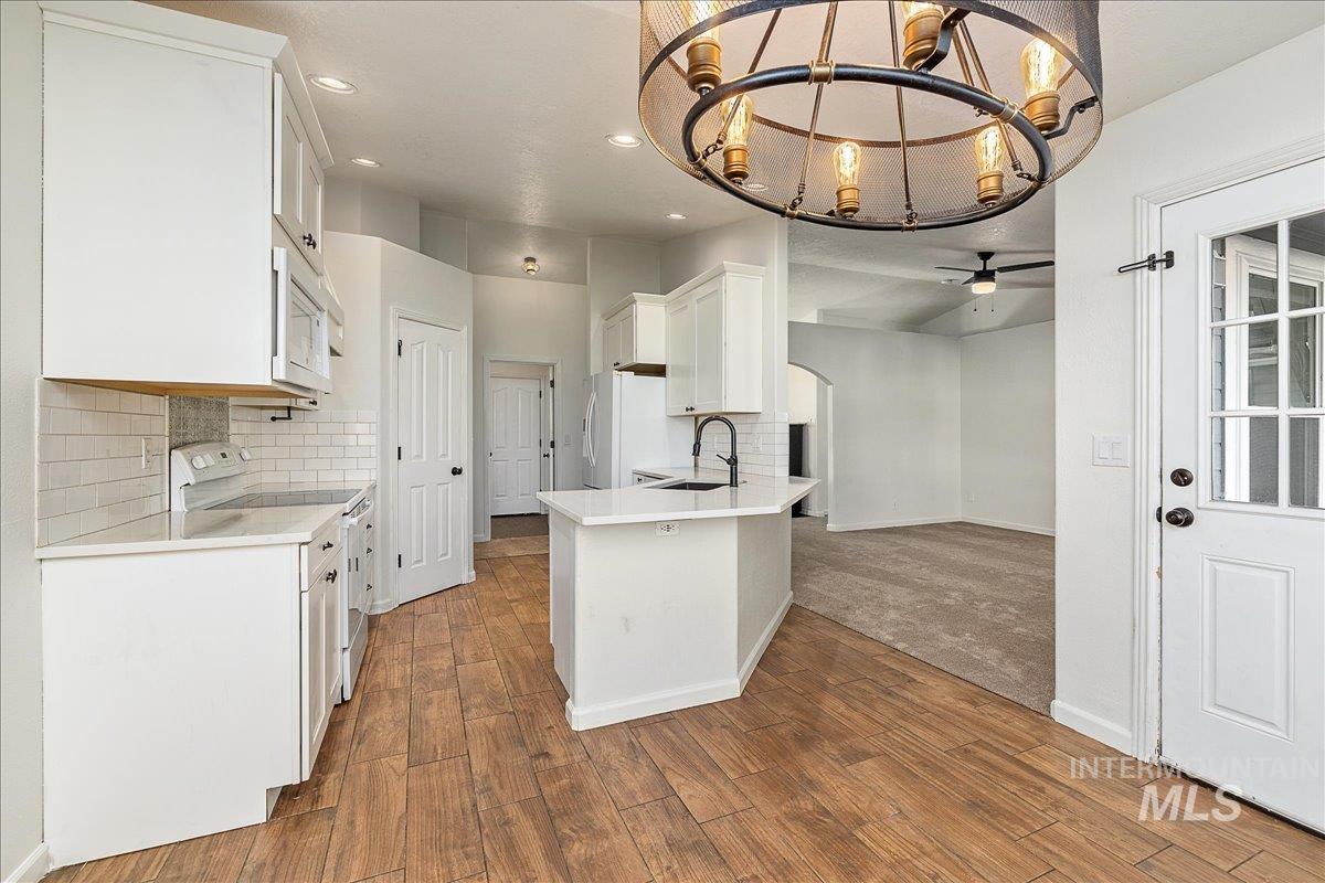 Kitchen with white cabinets, decorative backsplash, white appliances, a chandelier, and arched walkways