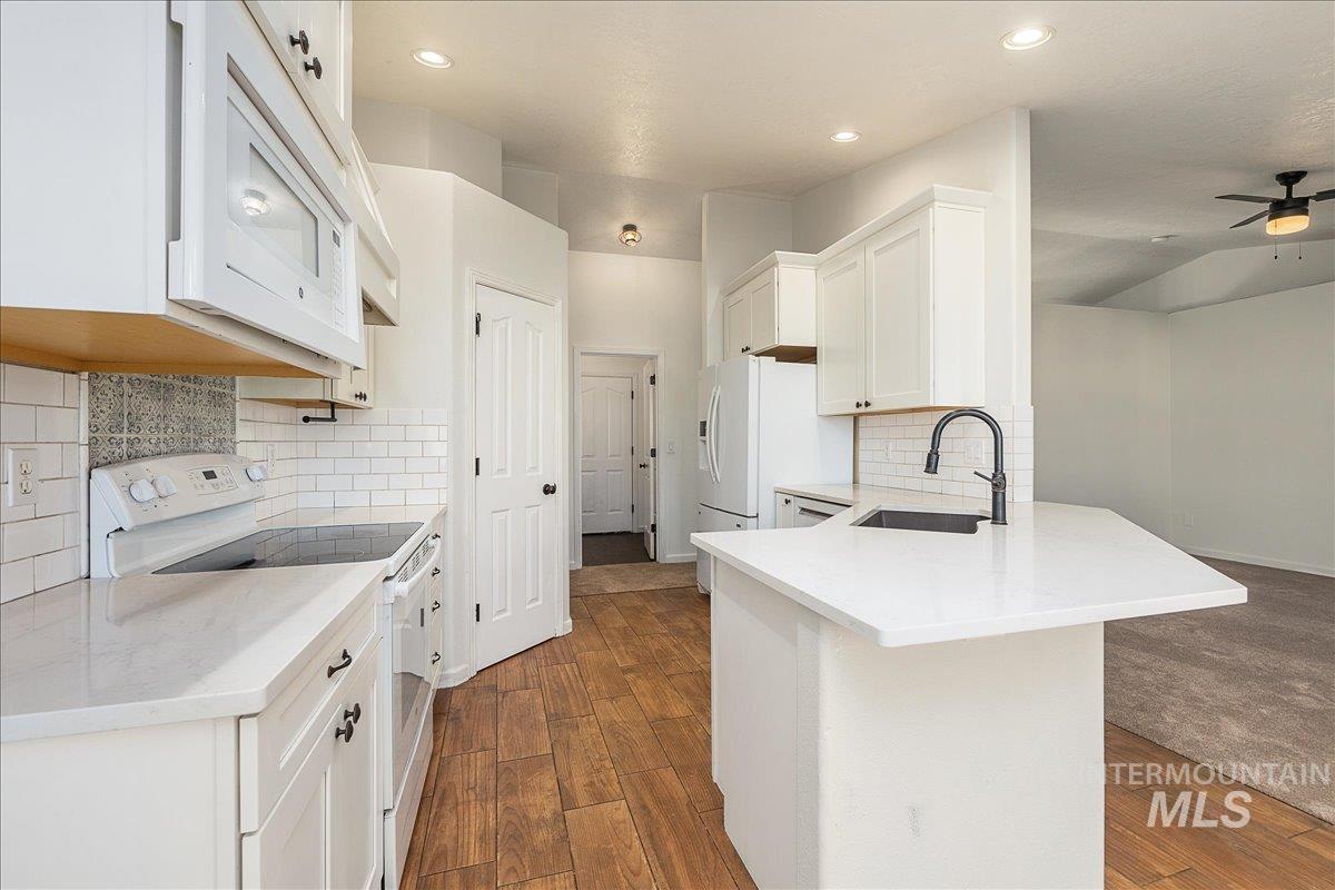 Kitchen featuring white appliances, white cabinets, a peninsula, light stone counters, and lofted ceiling