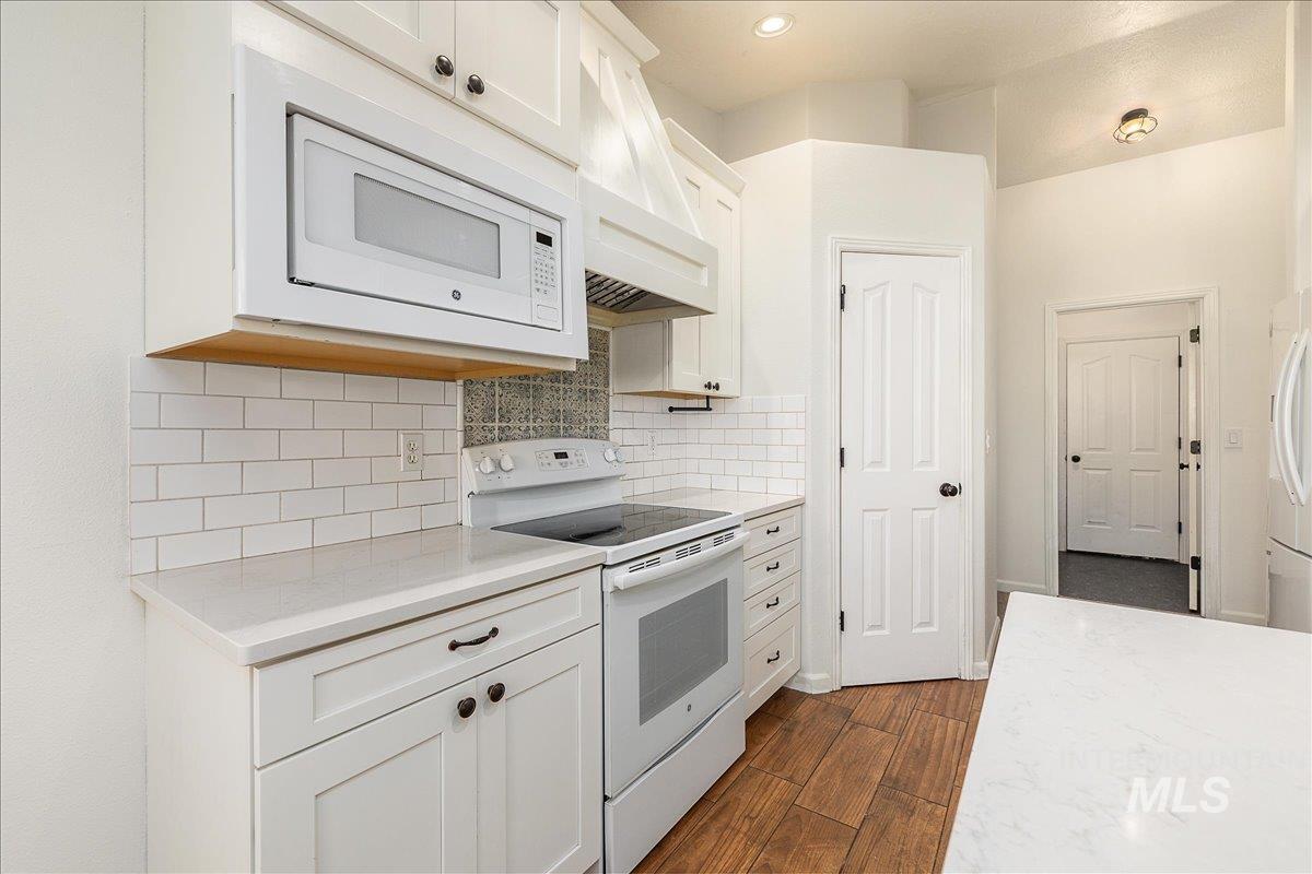Kitchen featuring white cabinetry, white appliances, custom exhaust hood, backsplash, and dark wood finished floors