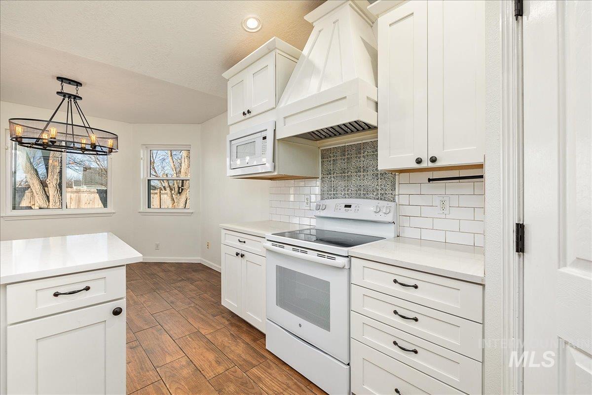 Kitchen with white appliances, decorative light fixtures, white cabinetry, custom range hood, and wood tiled floors