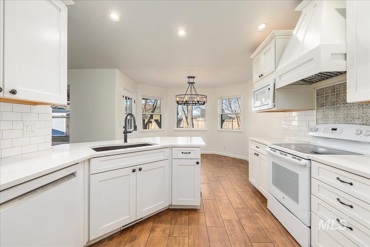 Kitchen with tasteful backsplash, white appliances, custom exhaust hood, white cabinetry, and light wood-style floors