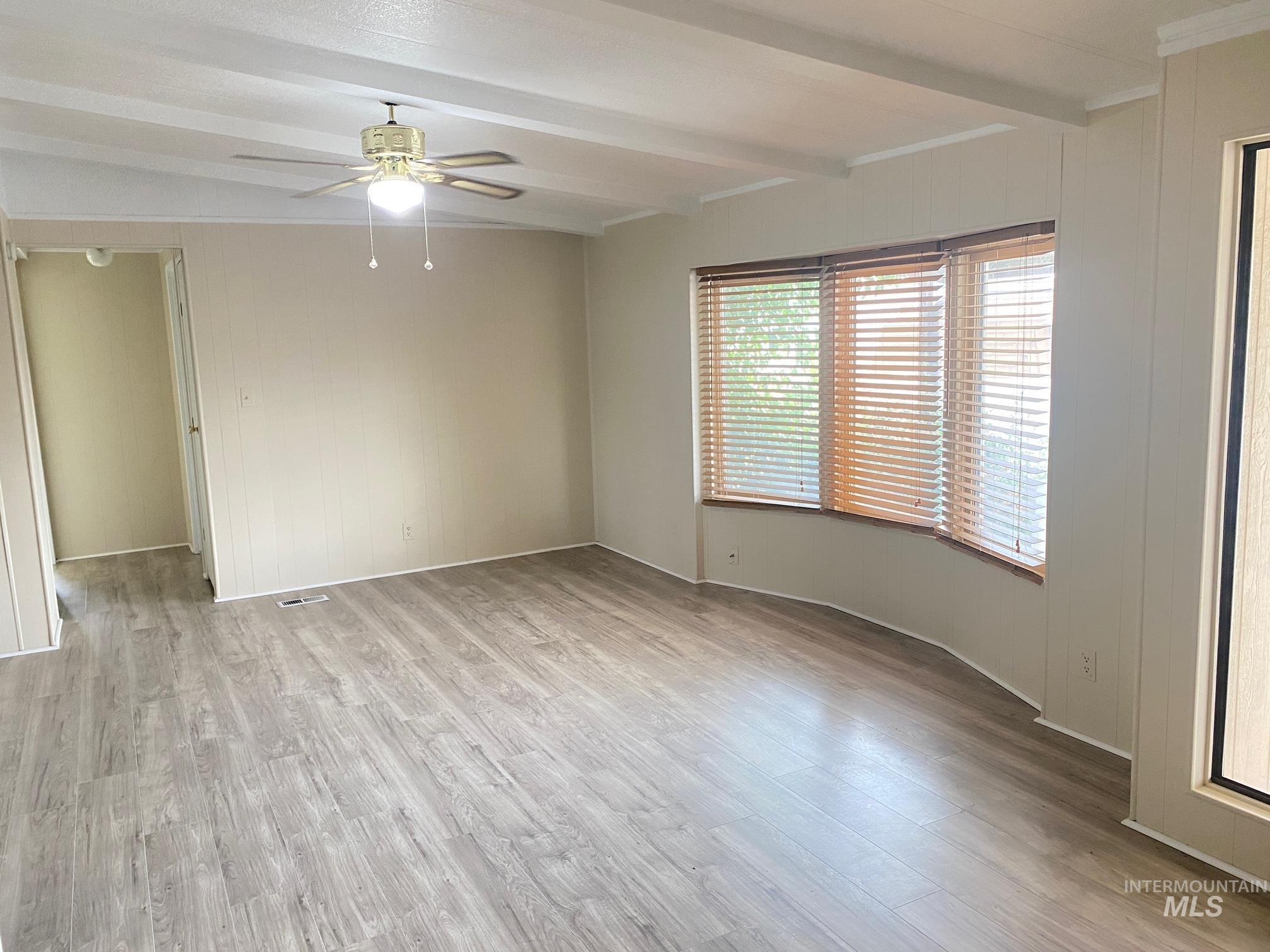 Living room with light wood-type flooring, wood walls, and a ceiling fan