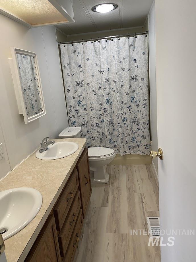 Bathroom featuring double vanity, a shower with shower curtain, and light wood-style flooring