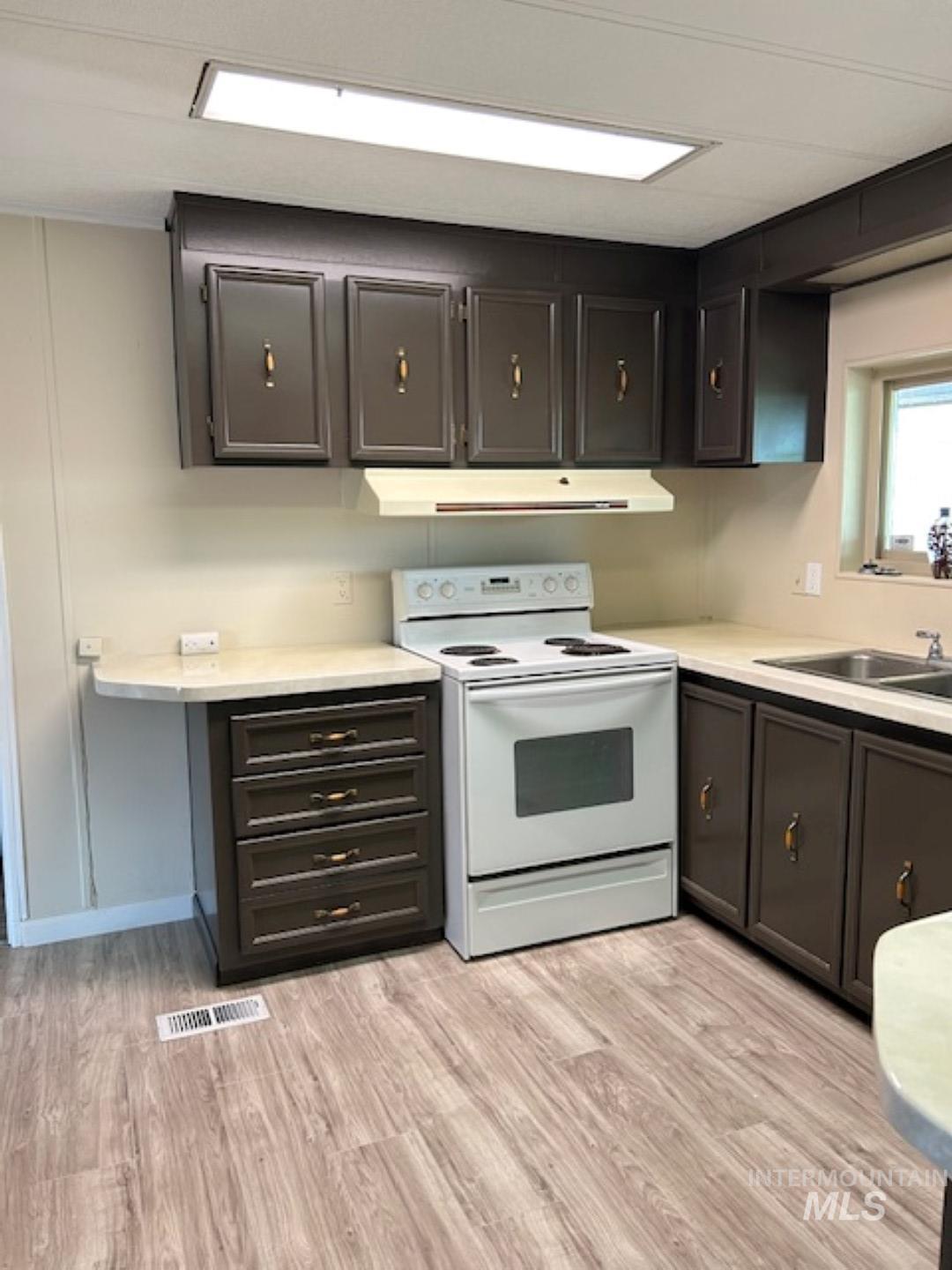 Kitchen featuring white electric range, light wood finished floors, light countertops, and under cabinet range hood
