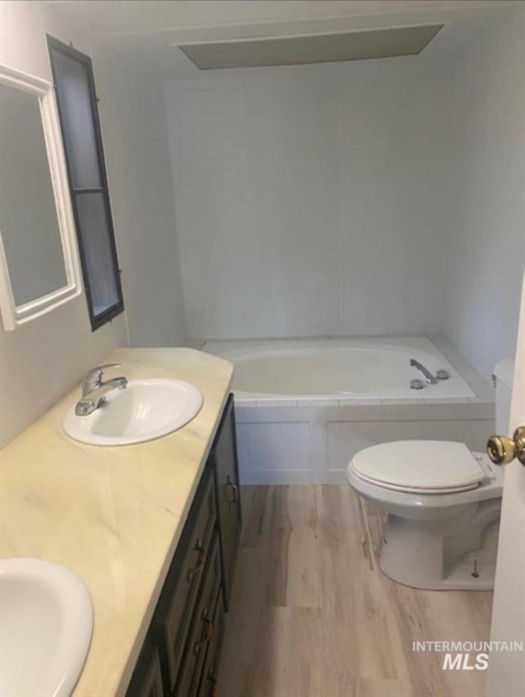 Bathroom with light wood finished floors, double vanity, and a garden tub