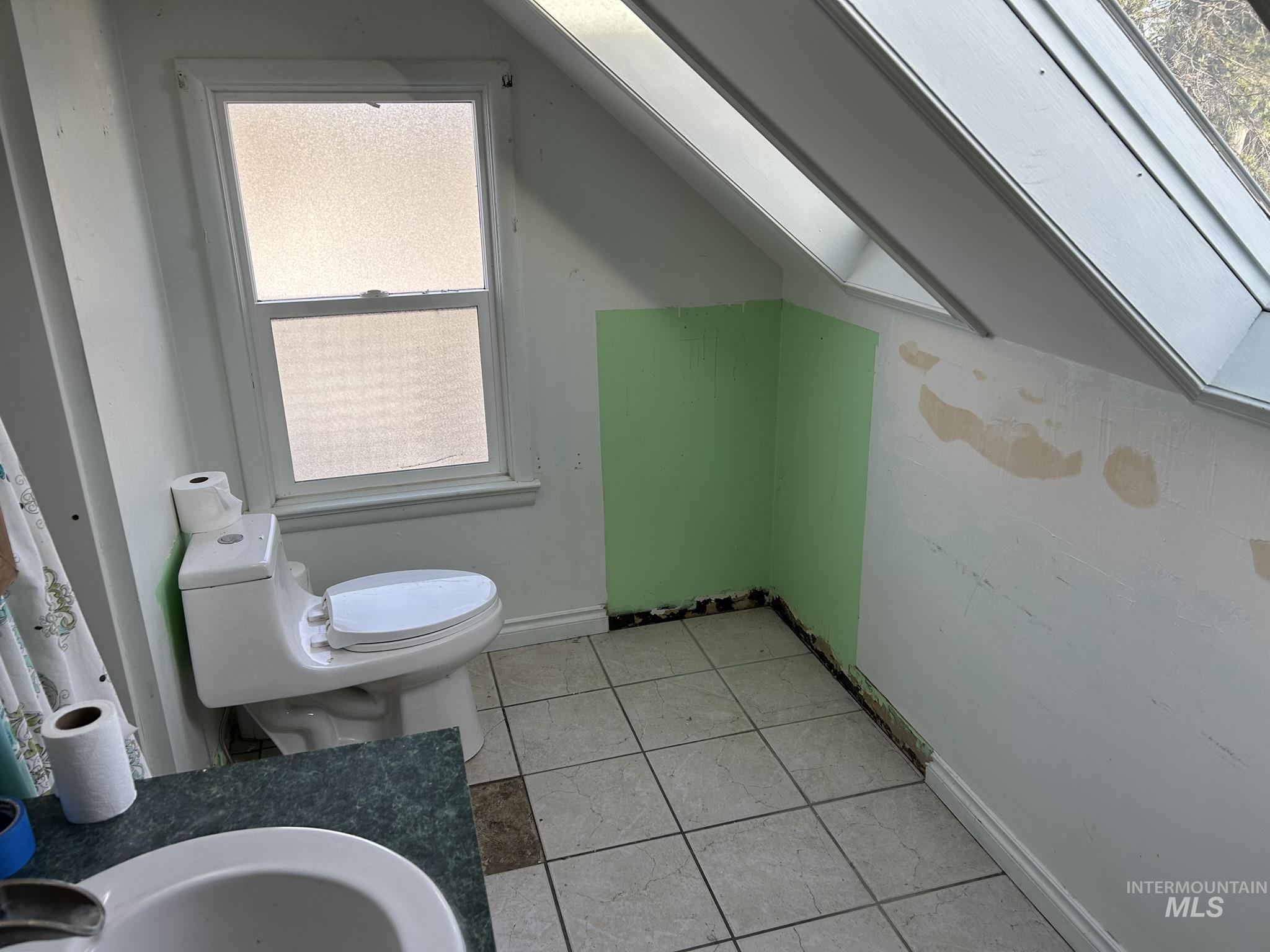 Bathroom with vaulted ceiling, a skylight, and light tile patterned flooring