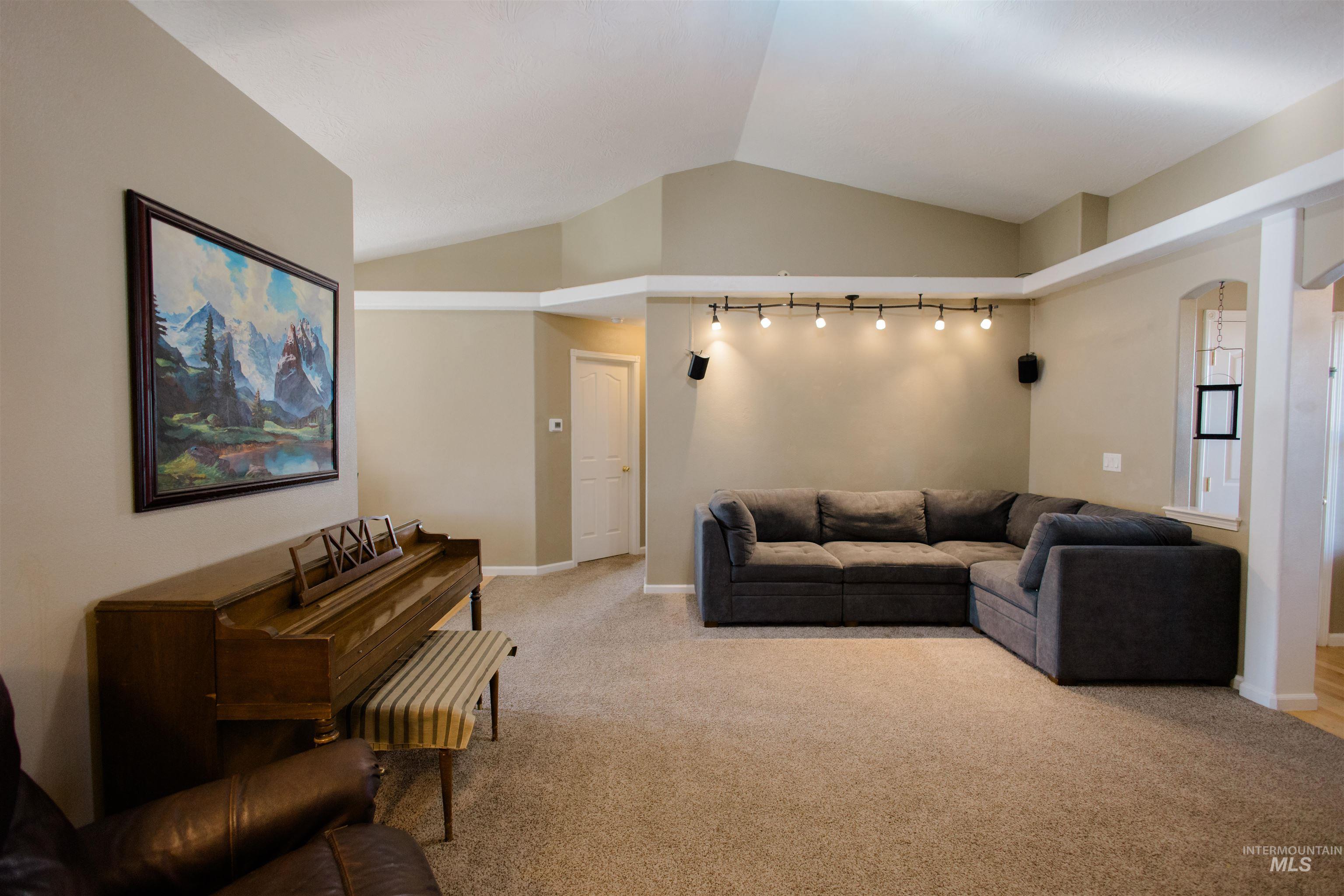 Living area with vaulted ceiling, light colored carpet, and arched walkways
