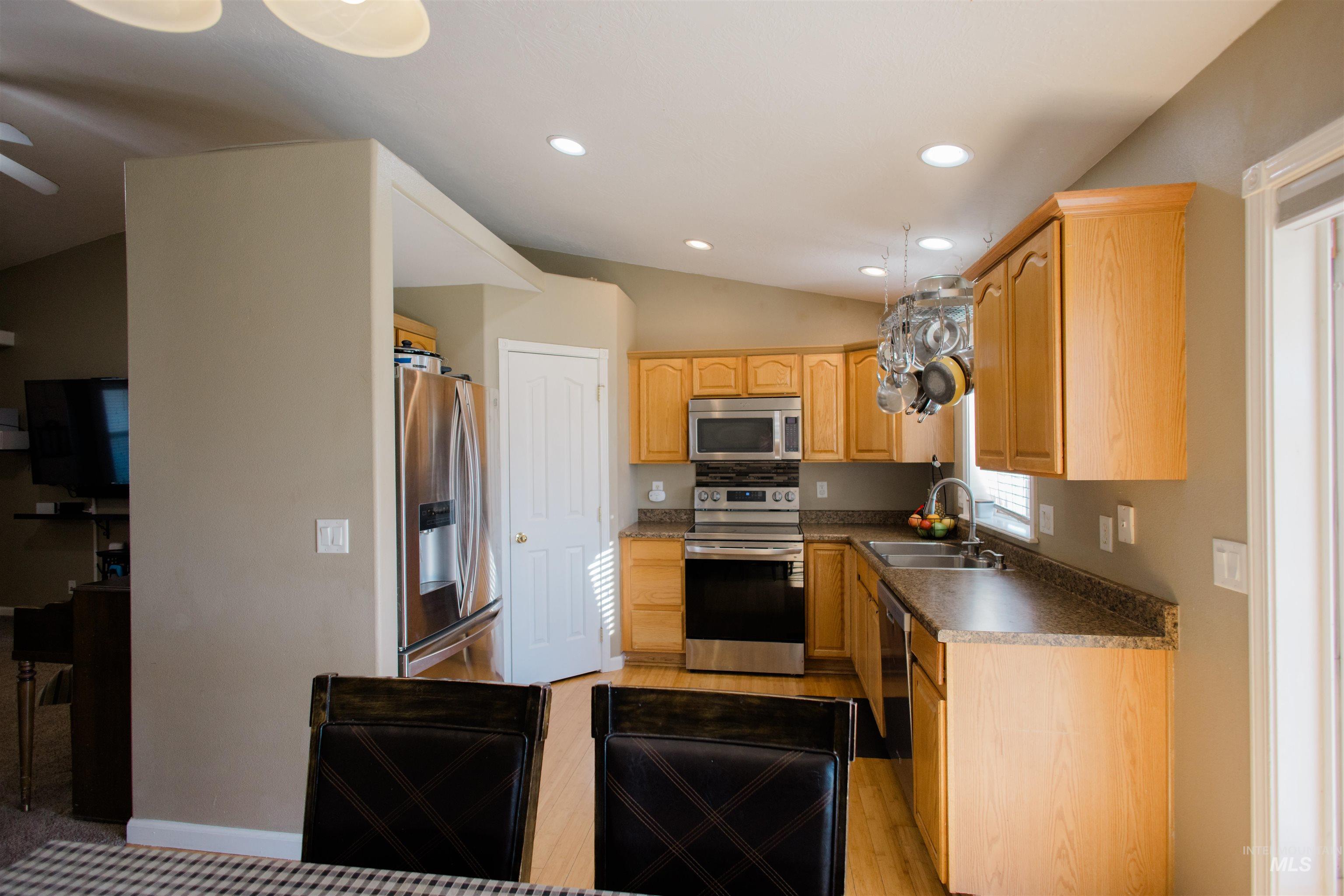 Kitchen with vaulted ceiling, dark countertops, appliances with stainless steel finishes, recessed lighting, and light wood-type flooring