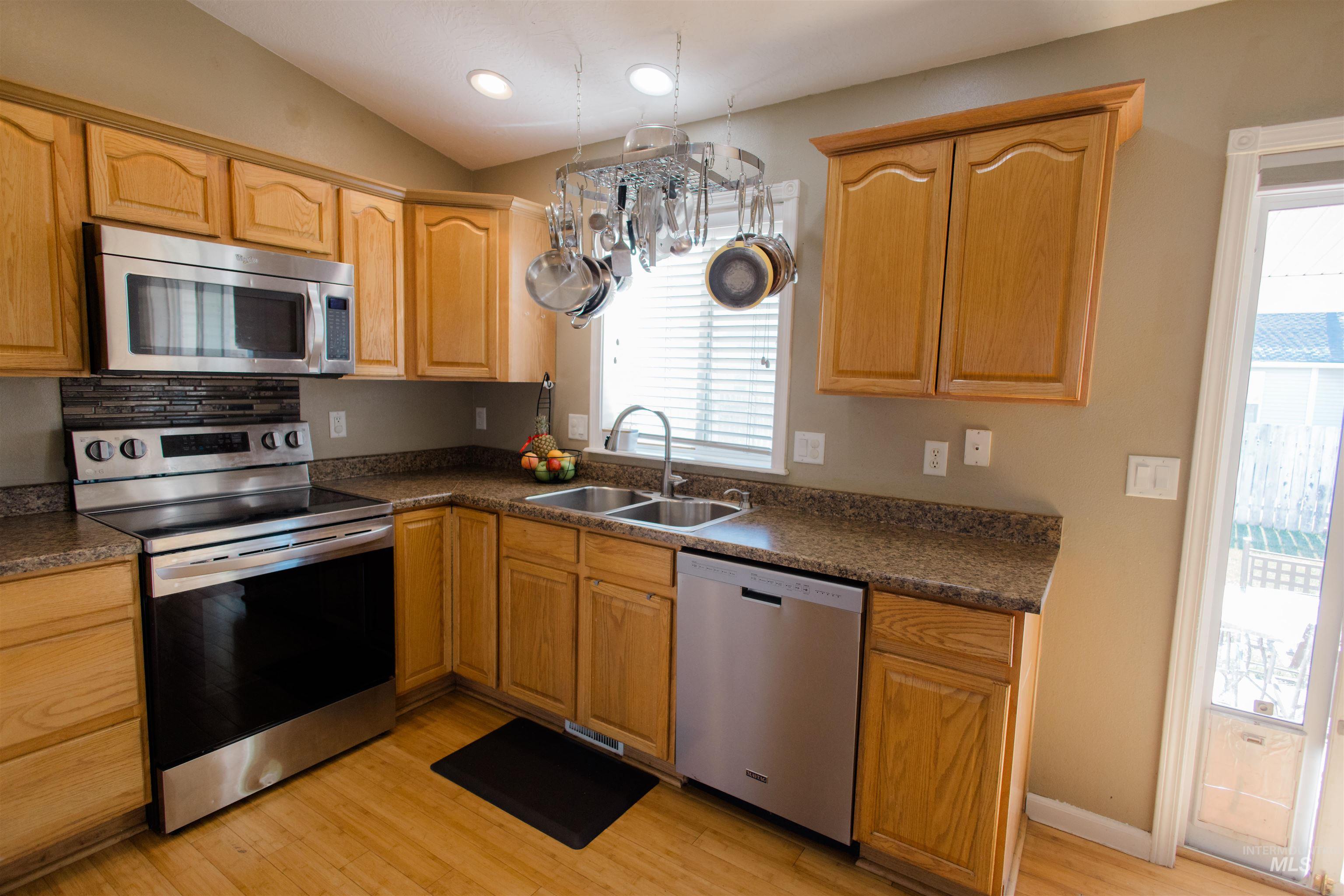 Kitchen featuring stainless steel appliances, dark countertops, light wood finished floors, vaulted ceiling, and recessed lighting