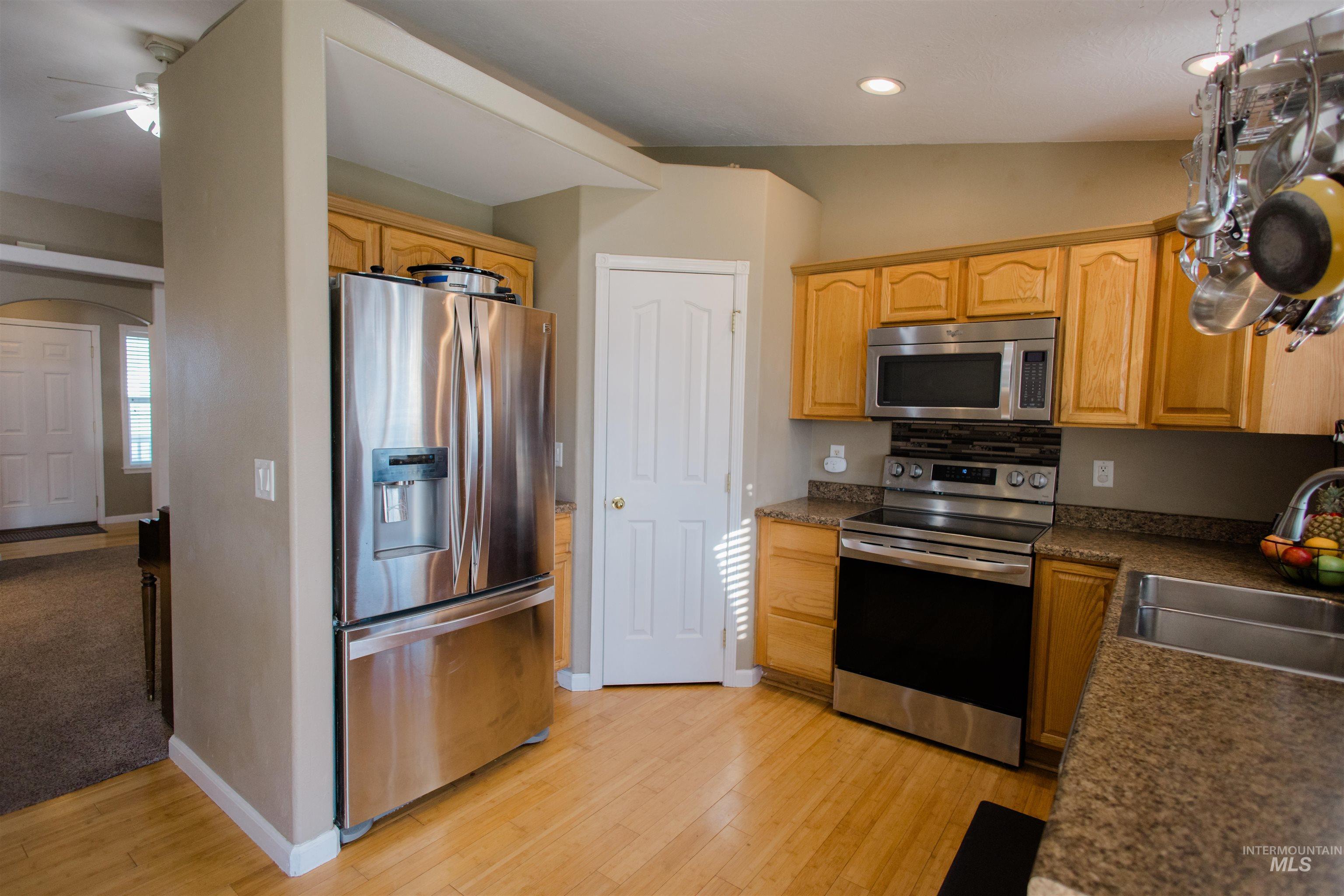 Kitchen featuring appliances with stainless steel finishes, arched walkways, light wood finished floors, light brown cabinets, and recessed lighting