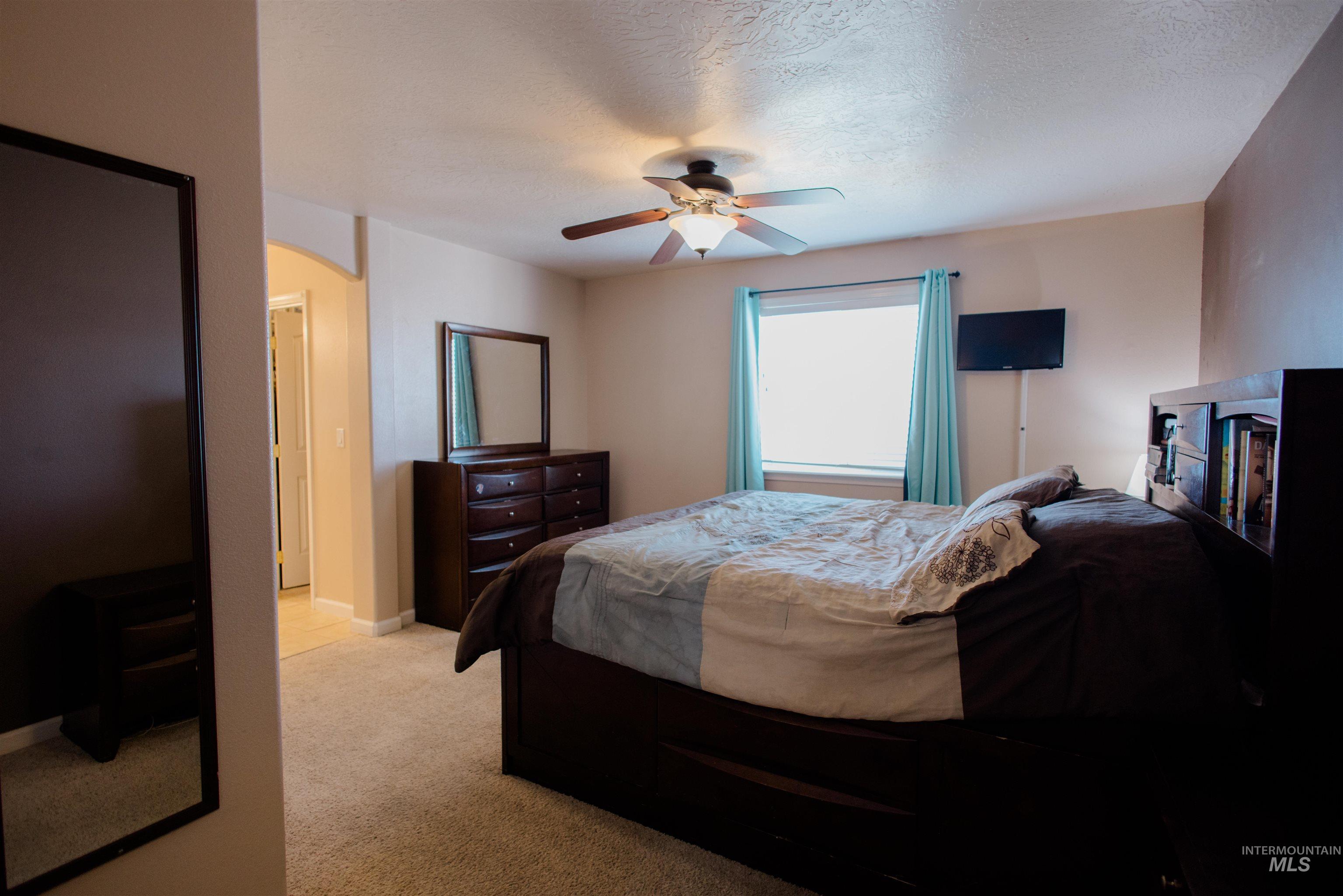 Bedroom with light carpet, ceiling fan, a textured ceiling, and arched walkways