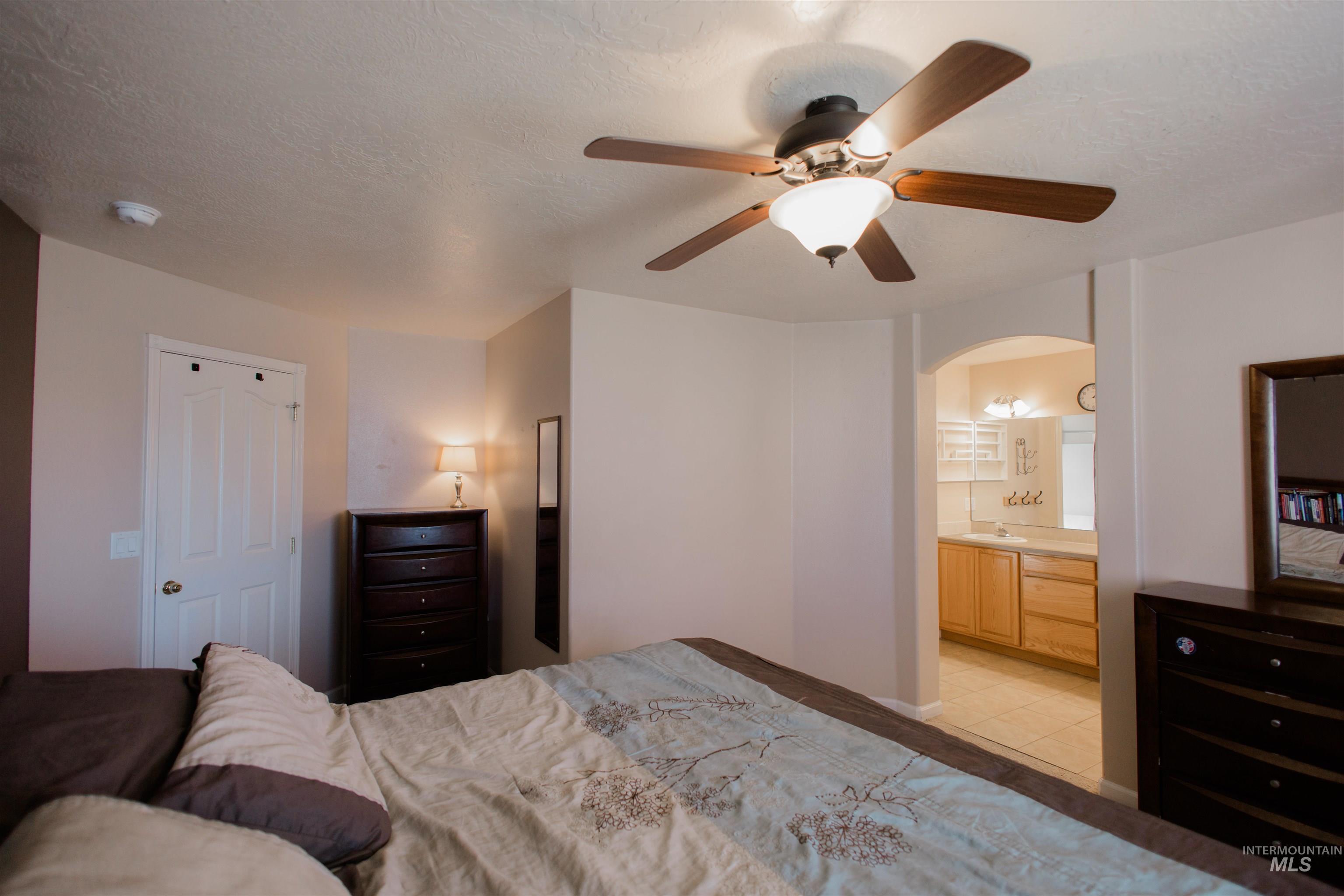 Bedroom with a textured ceiling, ceiling fan, arched walkways, and ensuite bathroom