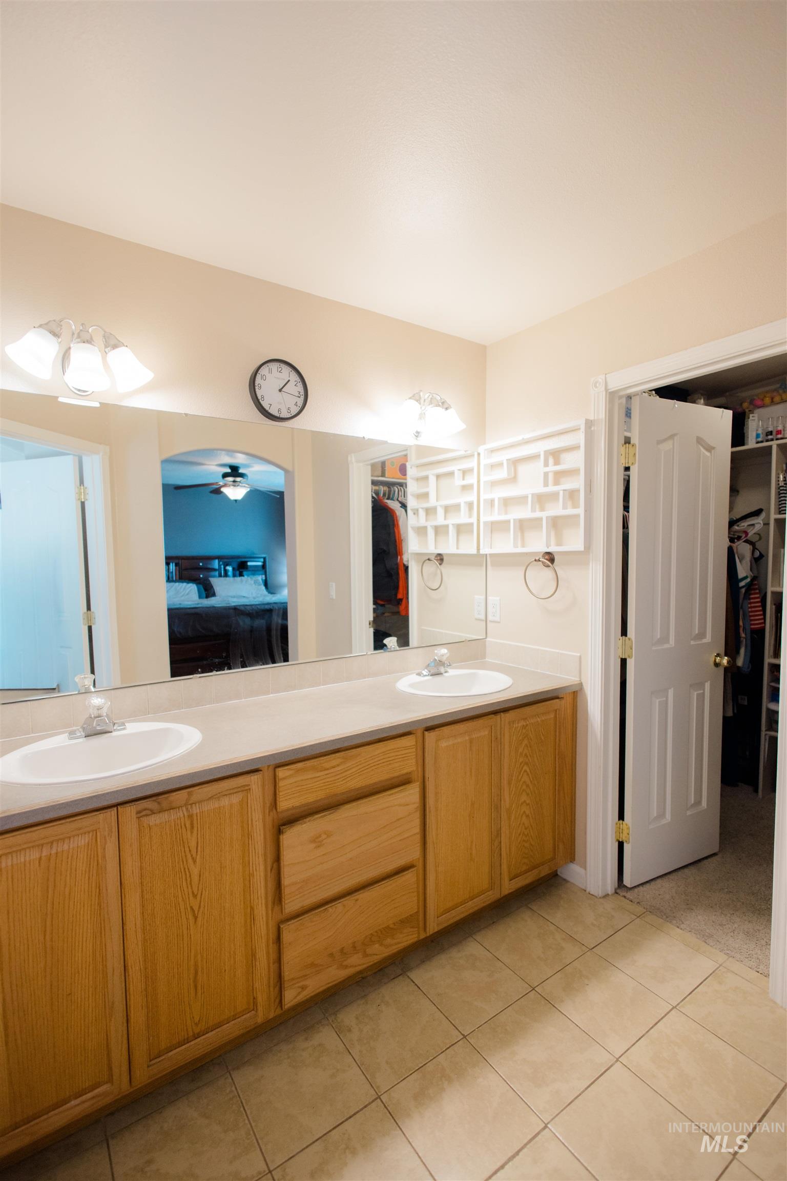 Ensuite bathroom with a spacious closet, double vanity, a ceiling fan, and light tile patterned flooring