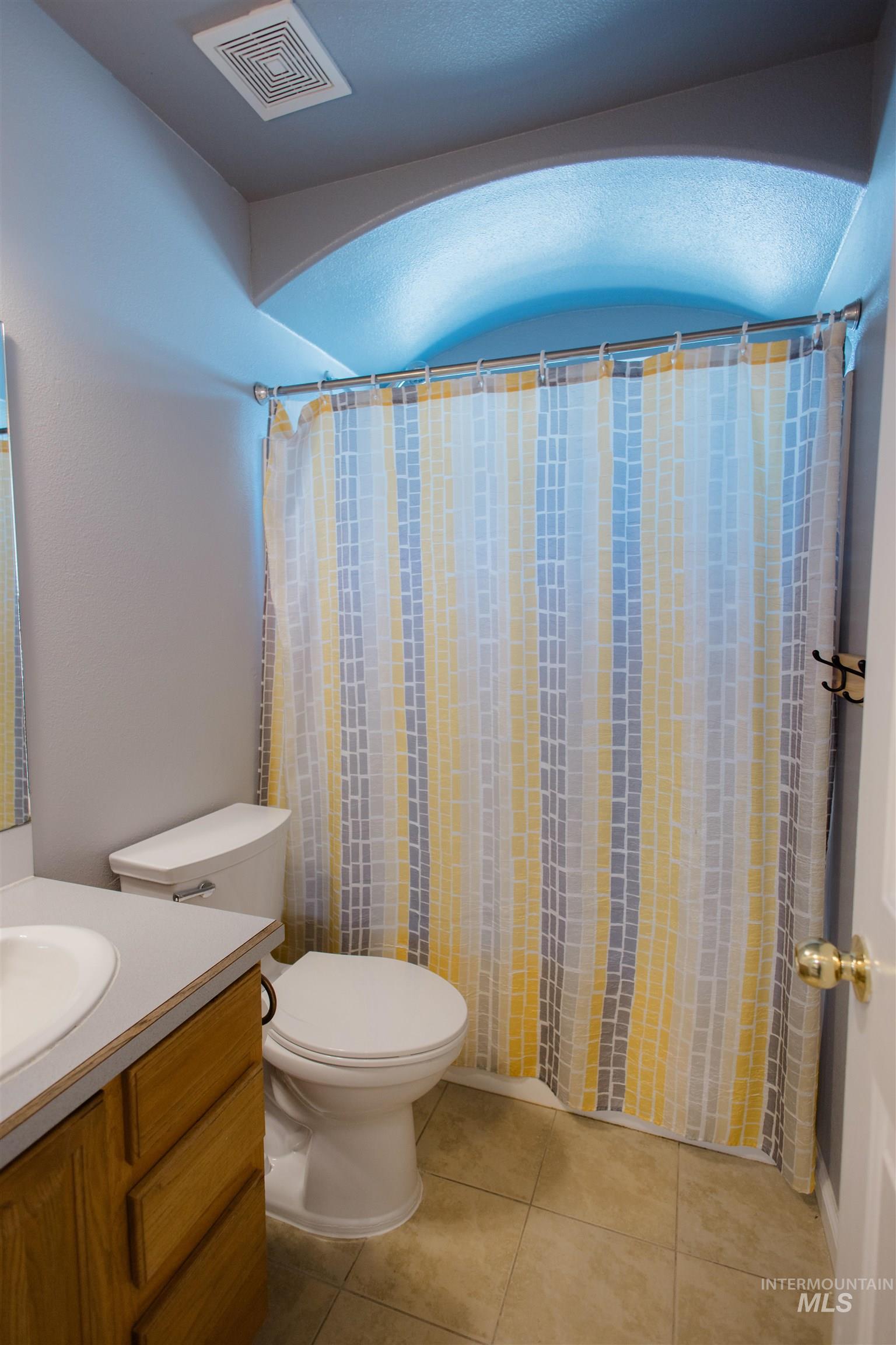 Full bath with a shower with curtain, vanity, vaulted ceiling, and light tile patterned floors
