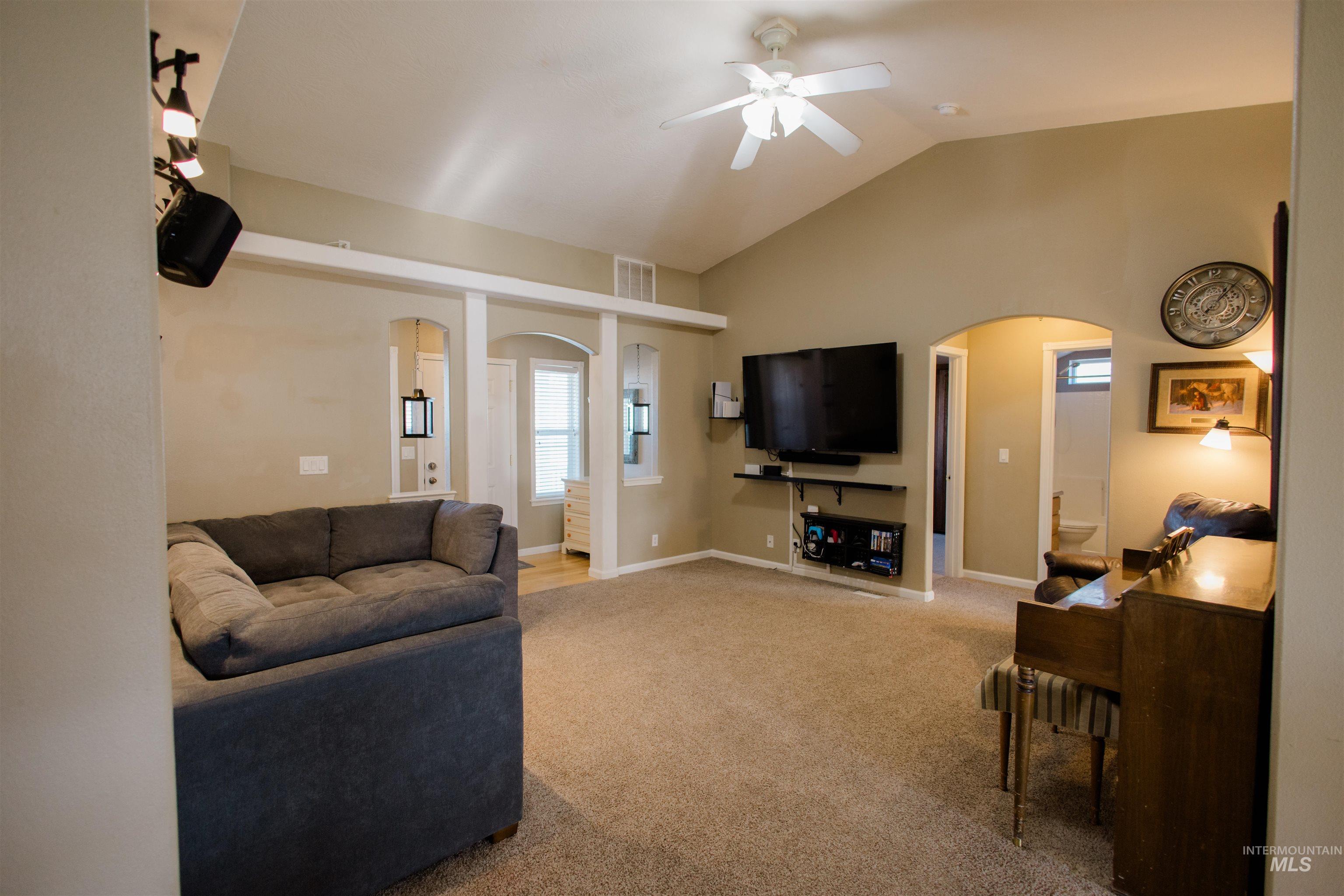 Living area featuring arched walkways, vaulted ceiling, carpet flooring, and ceiling fan