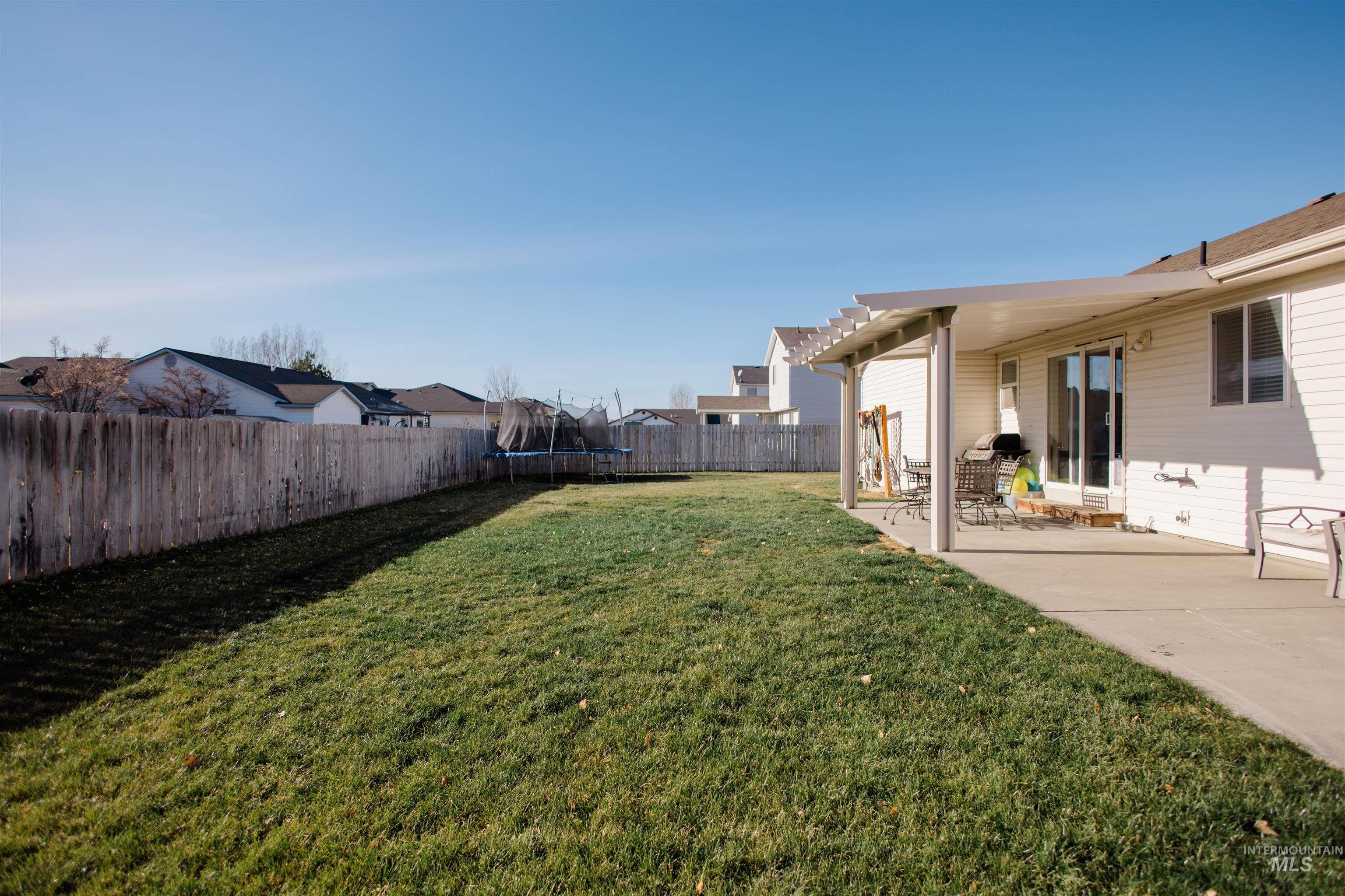 Fenced backyard featuring a patio area, a trampoline, and a residential view