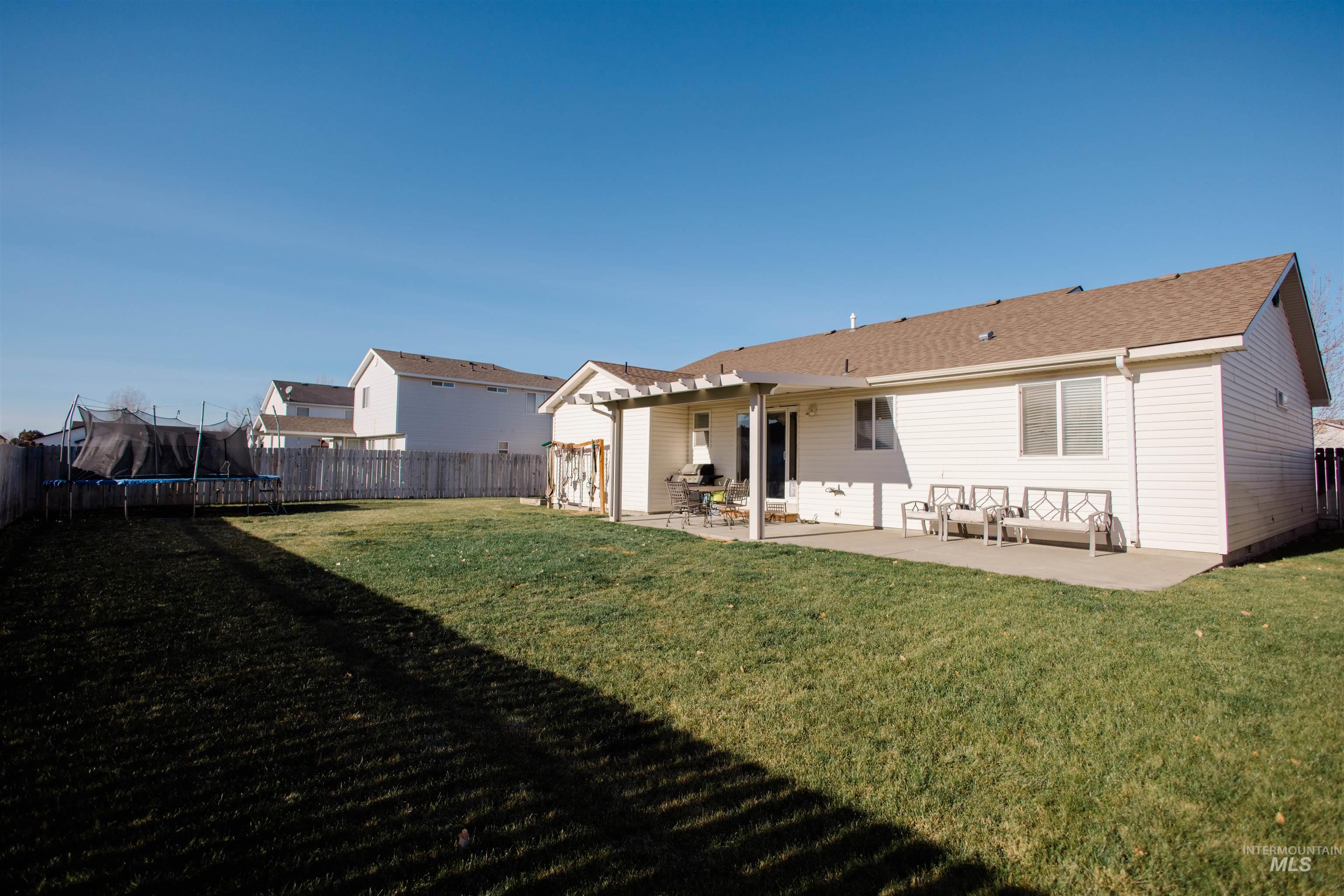Back of house featuring a patio, a trampoline, a fenced backyard, and a shingled roof