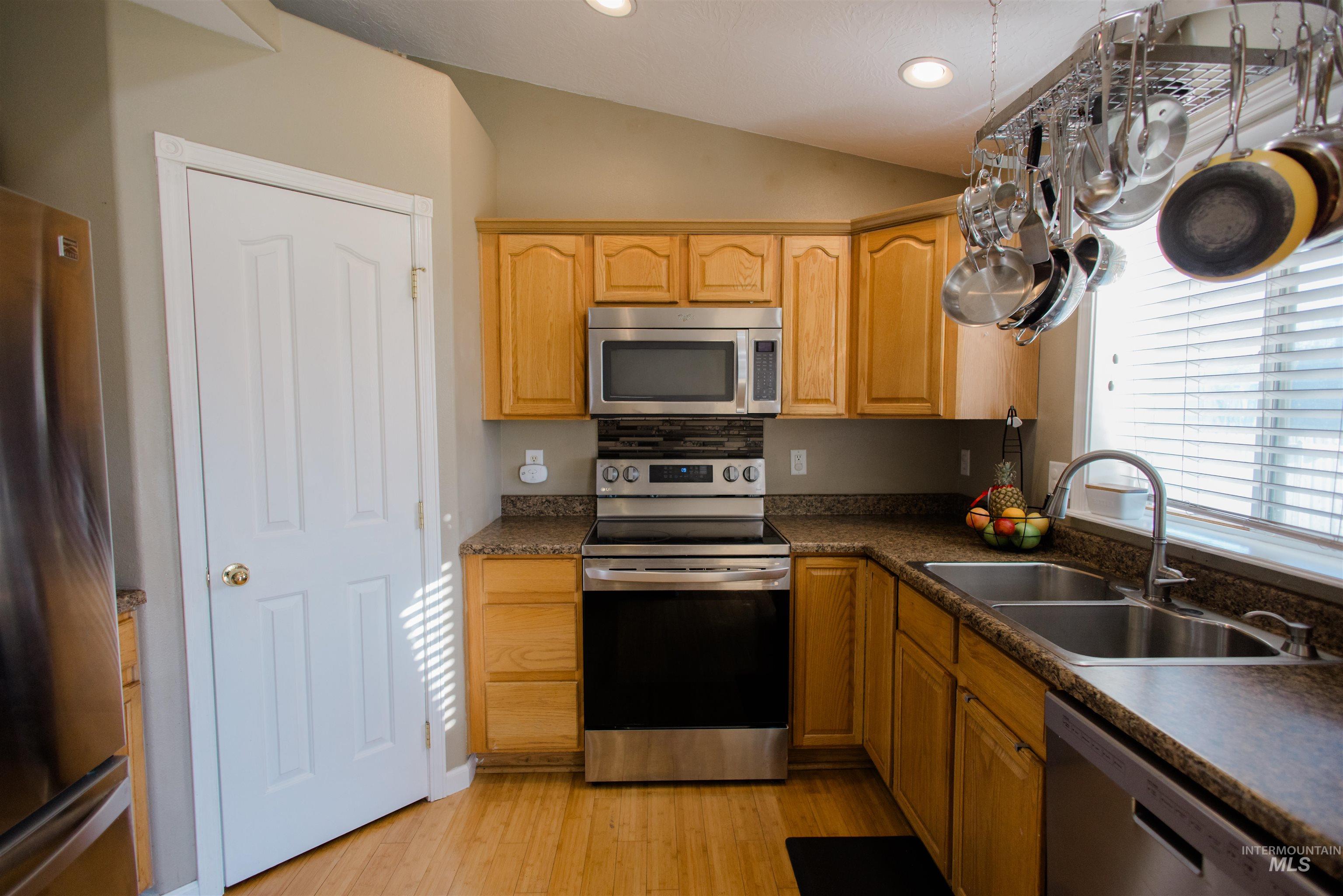 Kitchen with appliances with stainless steel finishes, lofted ceiling, light wood-style flooring, dark countertops, and recessed lighting