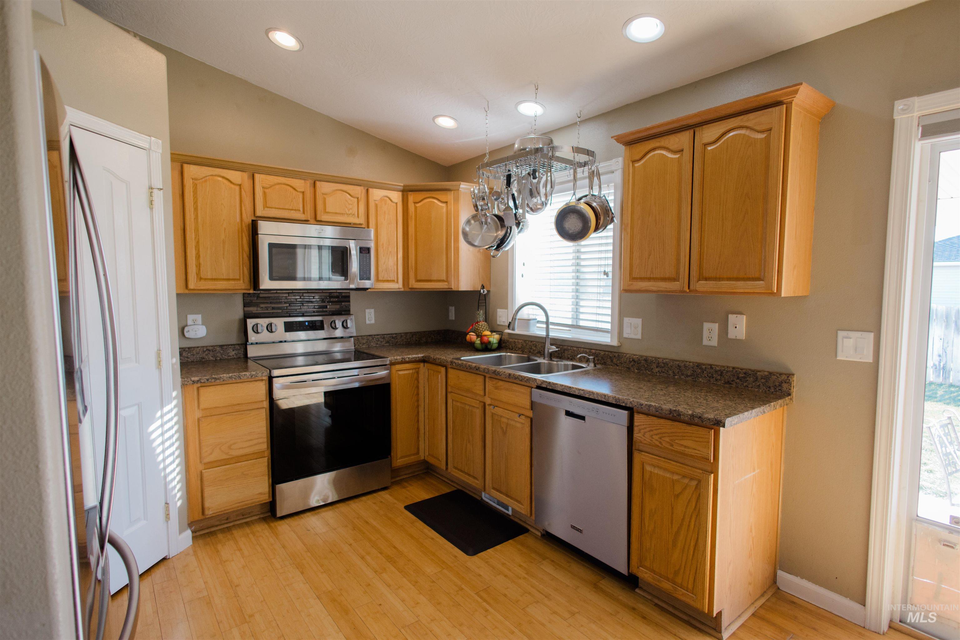 Kitchen featuring appliances with stainless steel finishes, dark countertops, vaulted ceiling, recessed lighting, and light wood-type flooring