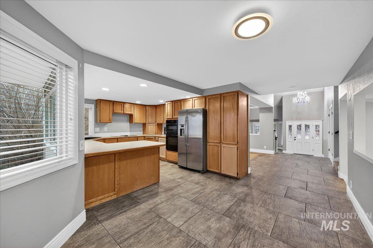 Kitchen with a peninsula, stainless steel fridge with ice dispenser, a chandelier, light countertops, and brown cabinetry