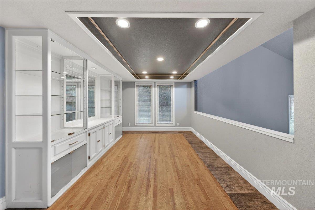 Unfurnished dining area with light wood-style floors, a raised ceiling, recessed lighting, and a textured ceiling