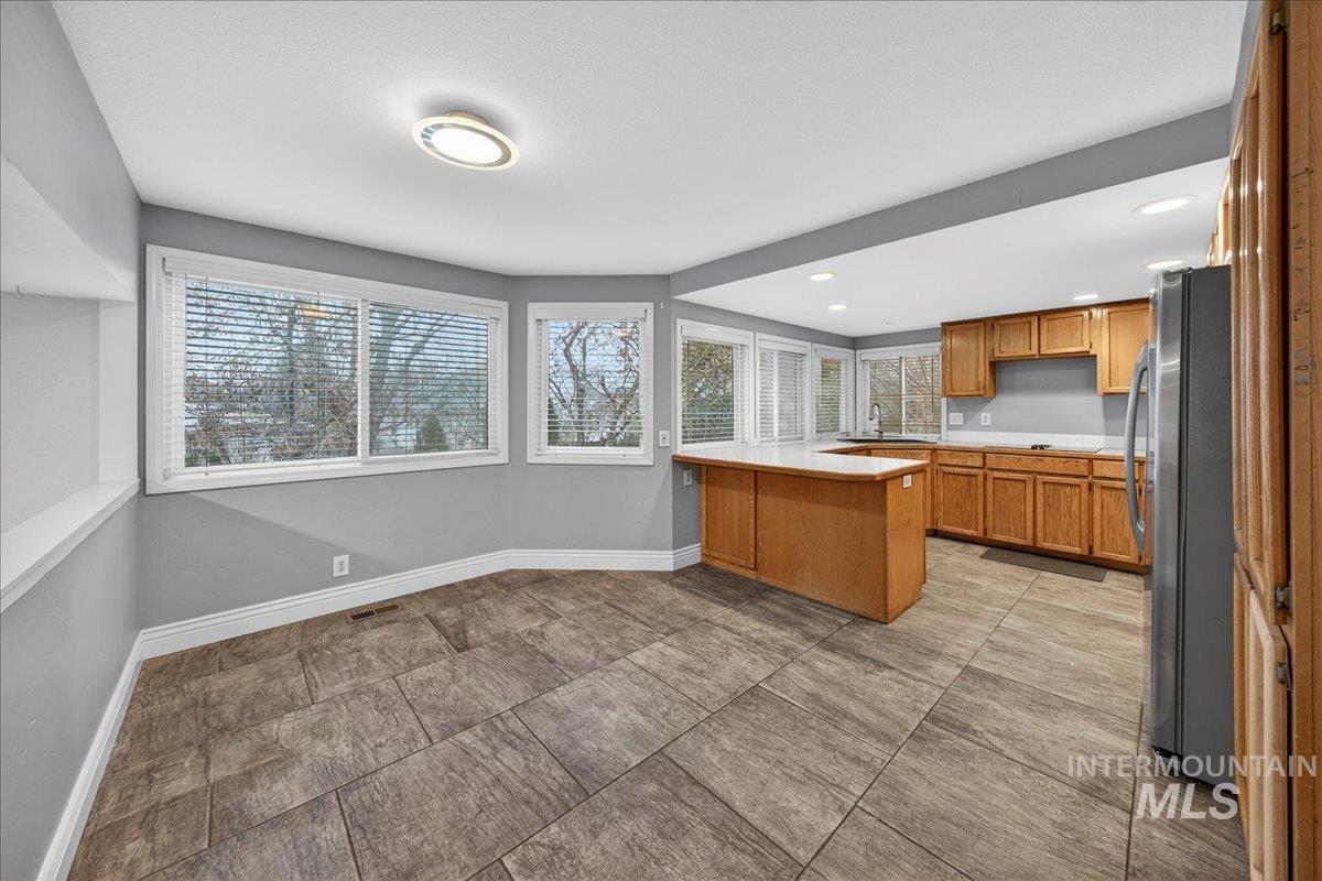 Kitchen with a peninsula, light countertops, brown cabinets, freestanding refrigerator, and healthy amount of natural light