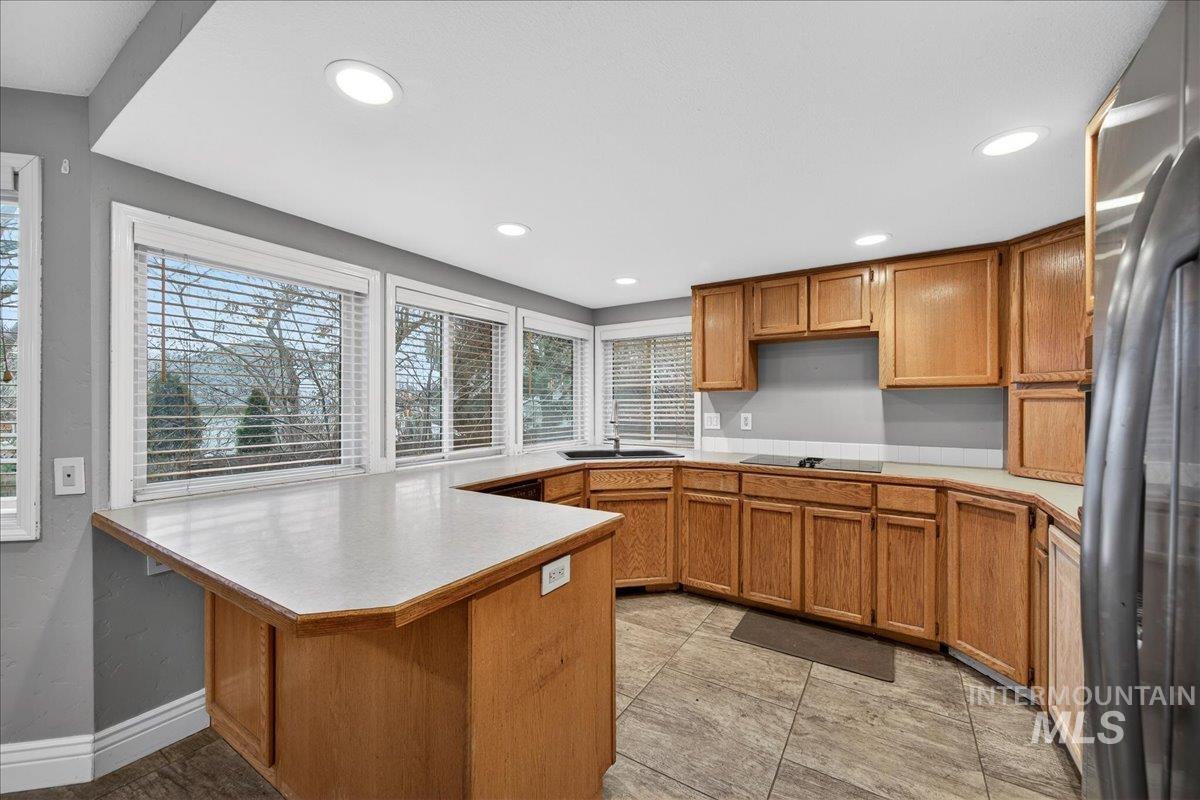 Kitchen with brown cabinetry, light countertops, freestanding refrigerator, and recessed lighting