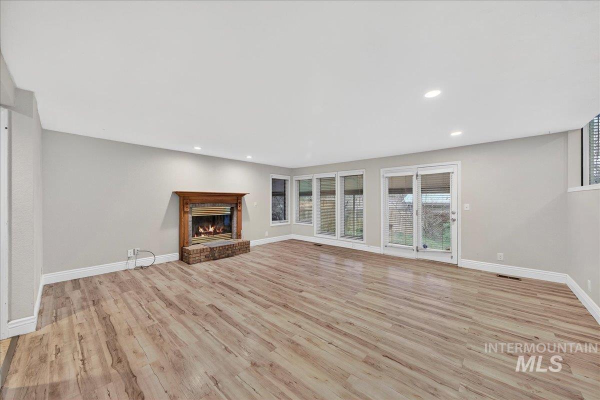 Unfurnished living room featuring light wood-style floors, recessed lighting, and a brick fireplace
