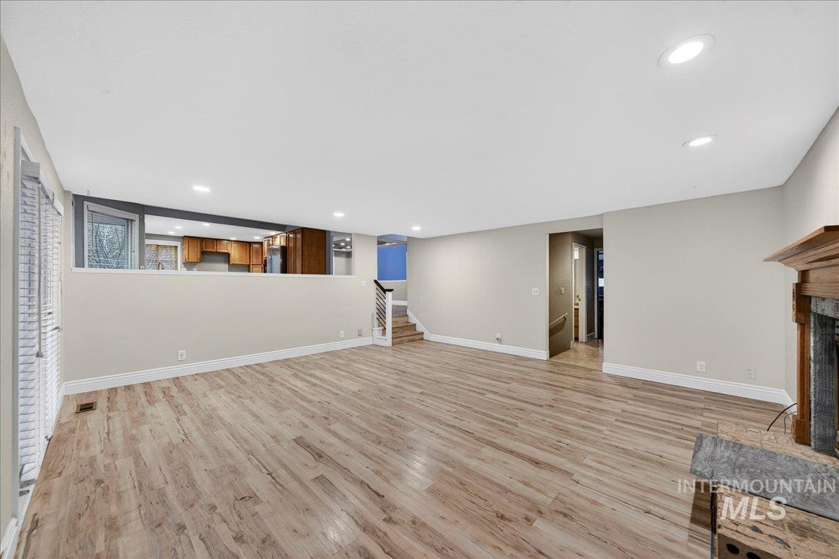 Unfurnished living room with light wood-style floors, a fireplace with raised hearth, recessed lighting, and stairs