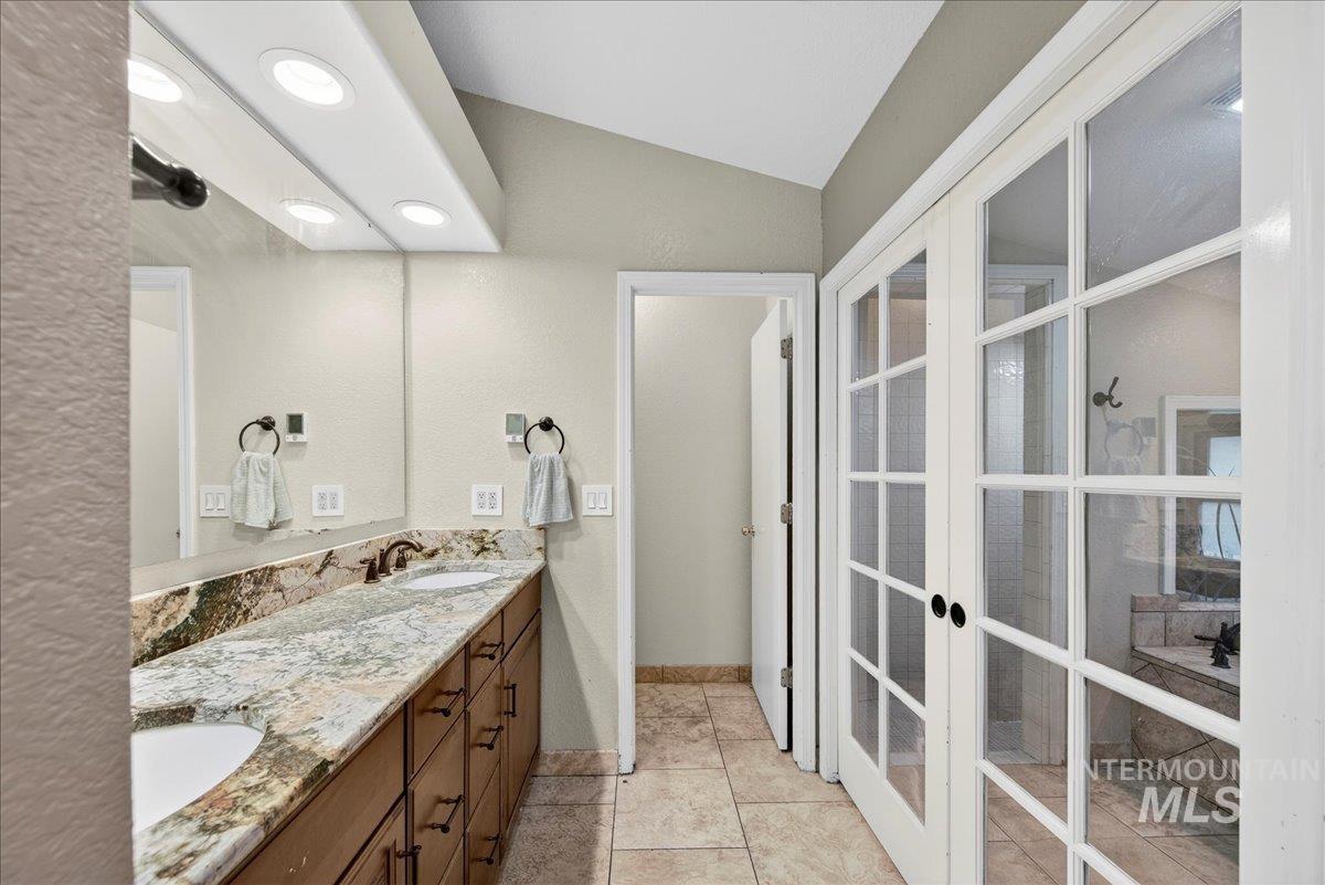 Full bath with double vanity, french doors, vaulted ceiling, and light tile patterned floors