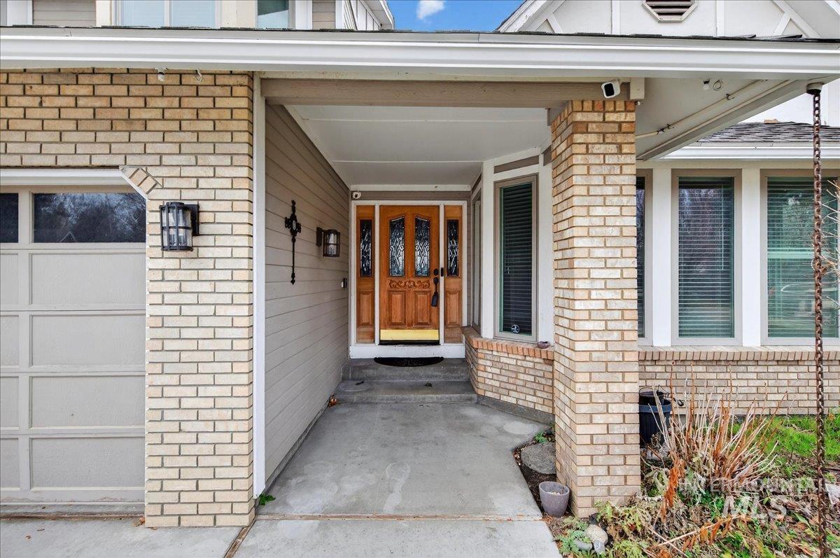 Entrance to property with brick siding, a porch, and a garage