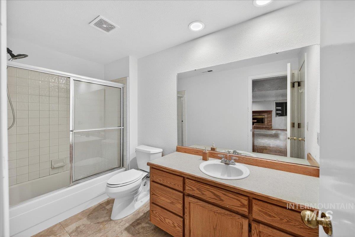 Bathroom with vanity, bath / shower combo with glass door, a textured wall, and a brick fireplace