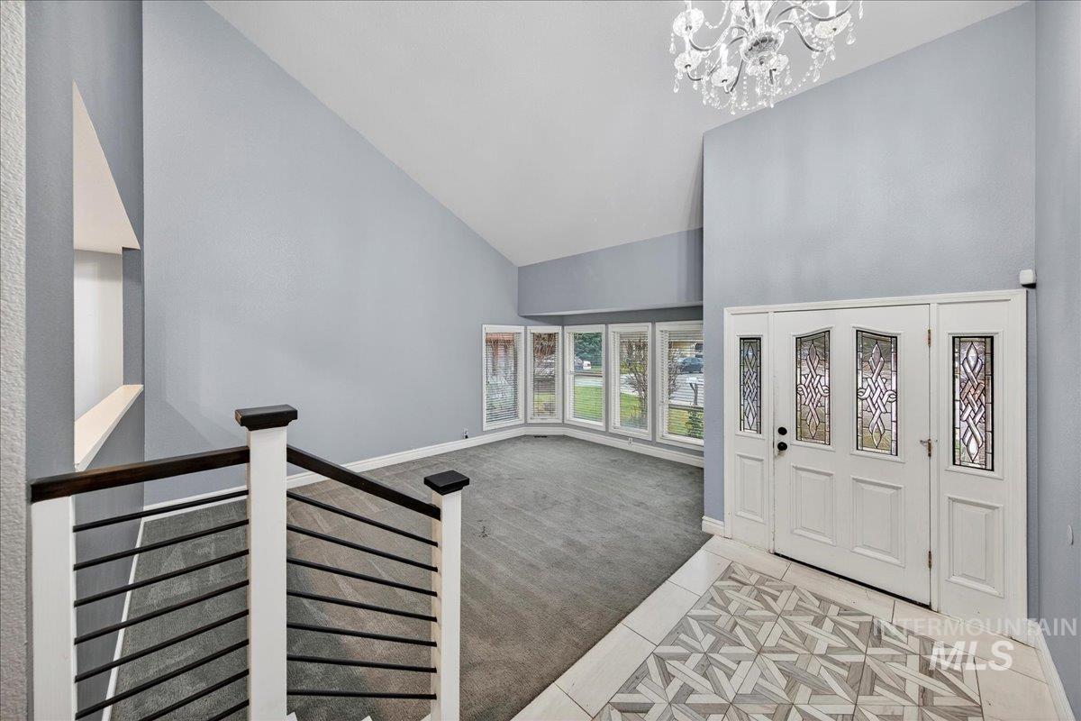 Foyer with light colored carpet, high vaulted ceiling, a chandelier, and light tile patterned floors