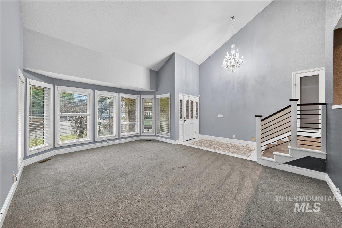 Unfurnished living room with high vaulted ceiling, a chandelier, carpet, and stairway