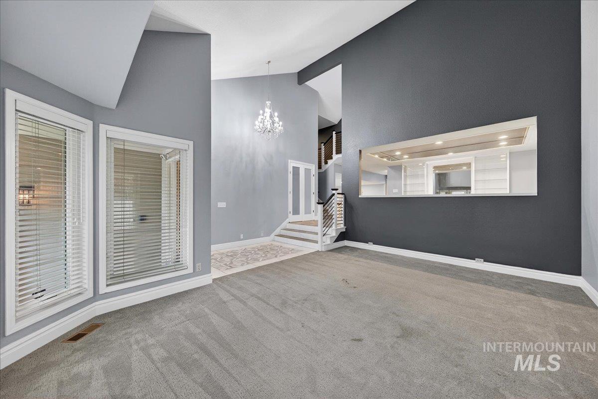 Unfurnished living room with light carpet, a chandelier, high vaulted ceiling, and stairs