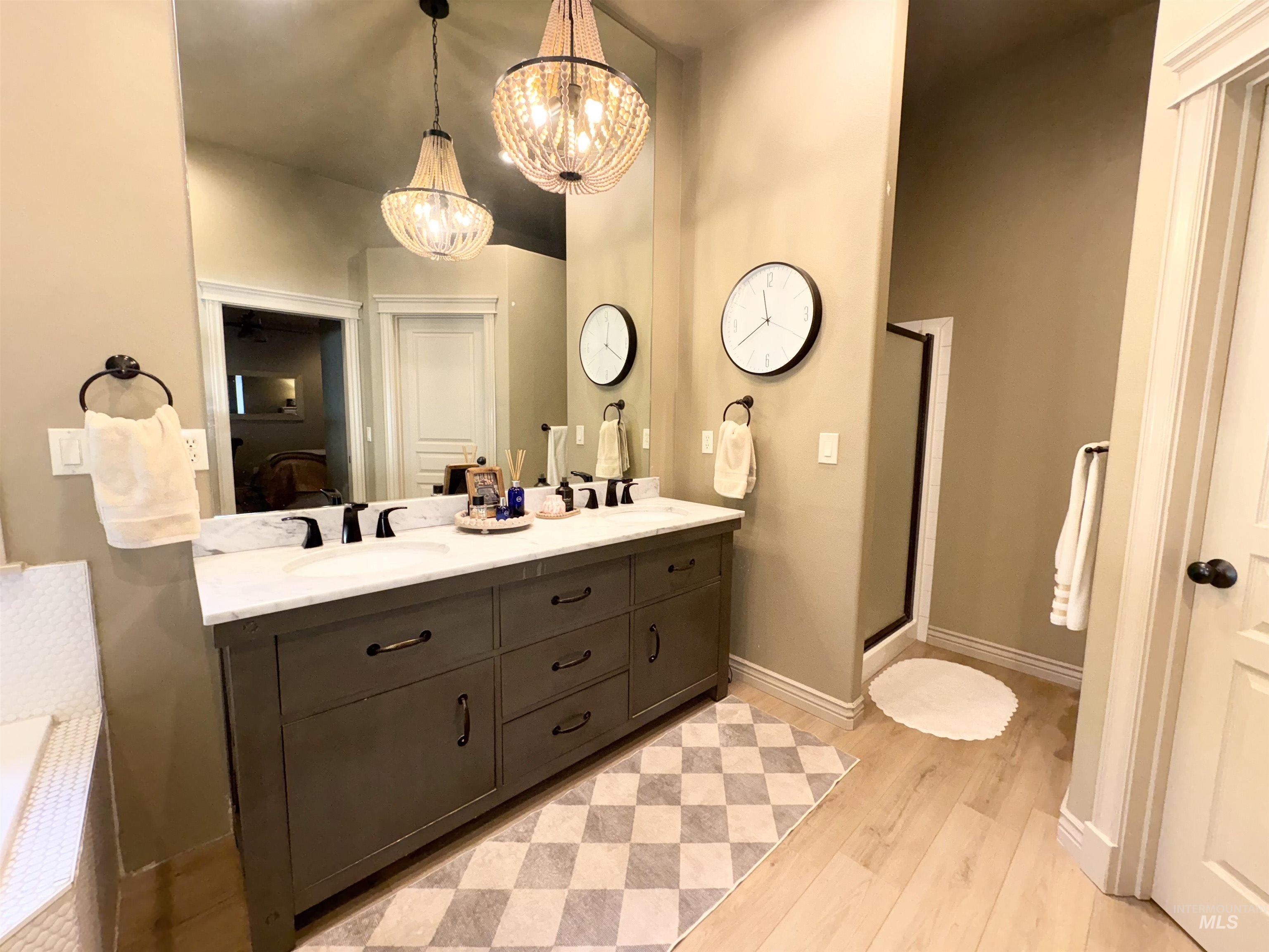 Ensuite bathroom with double vanity, light wood-style flooring, a shower stall, and a chandelier