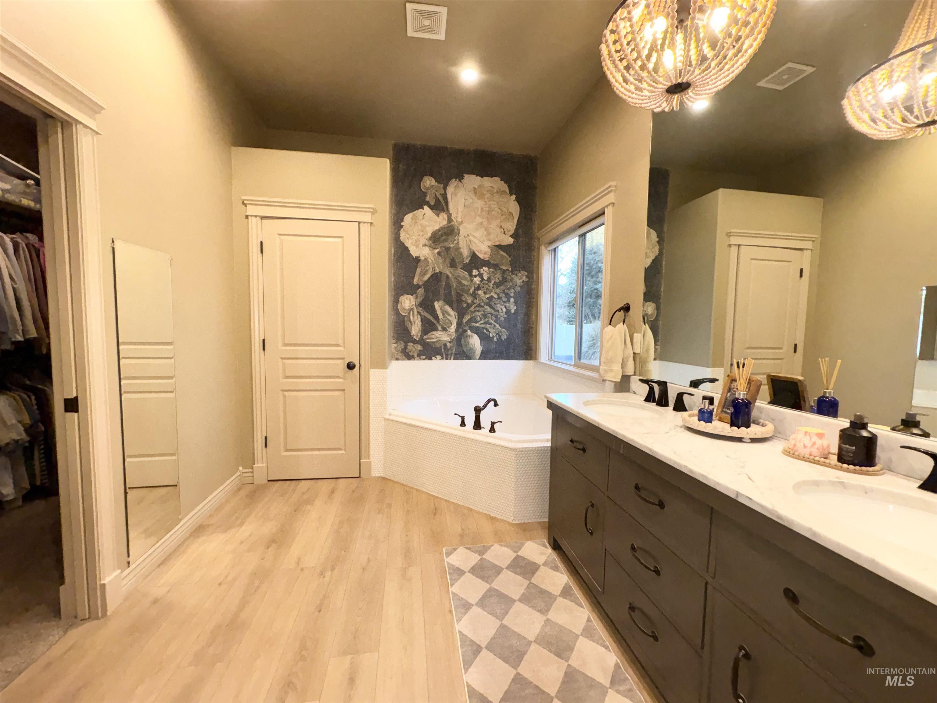 Bathroom featuring a garden tub, a walk in closet, double vanity, and light wood-style flooring