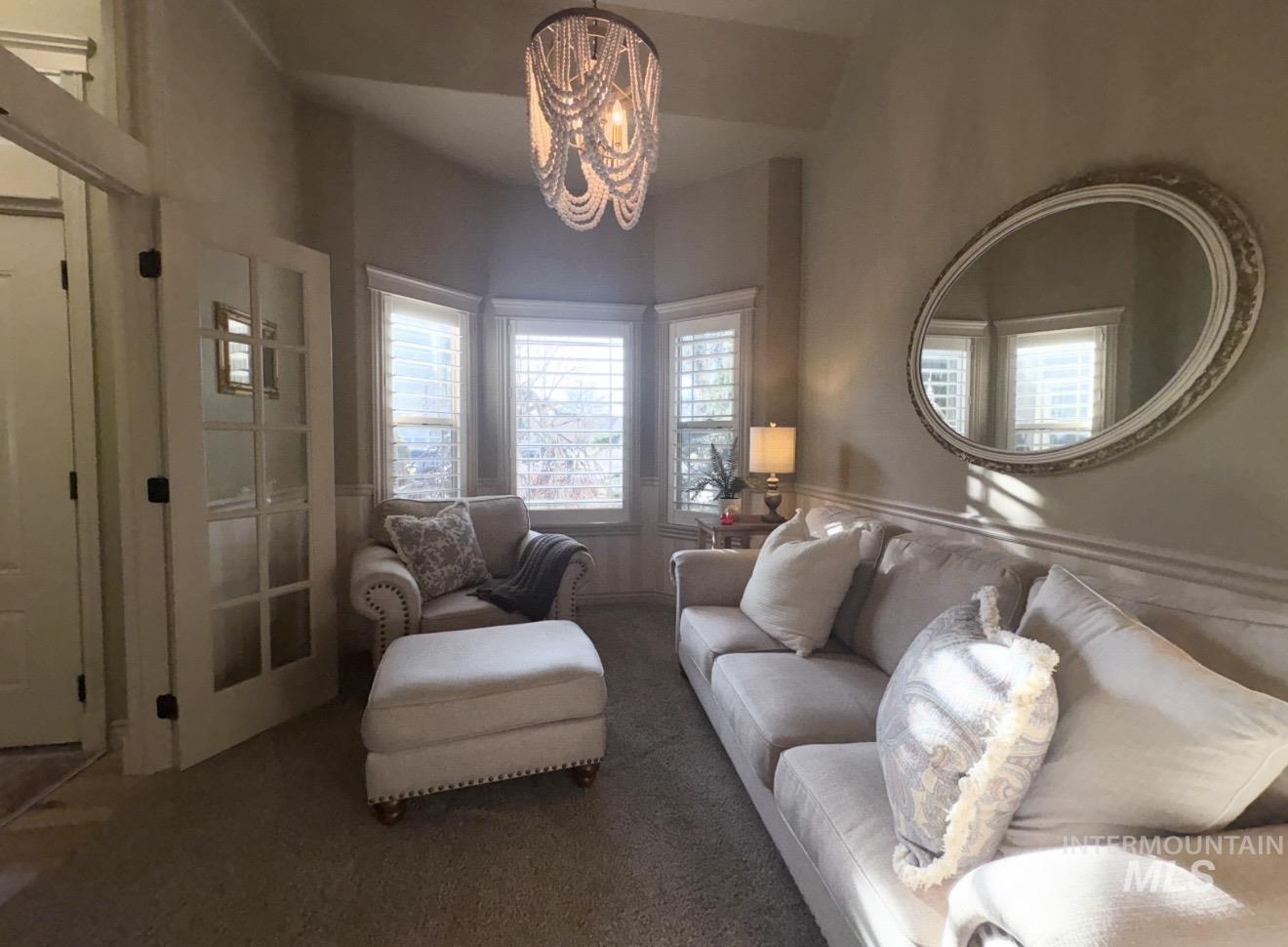Carpeted living area featuring a chandelier and a wainscoted wall