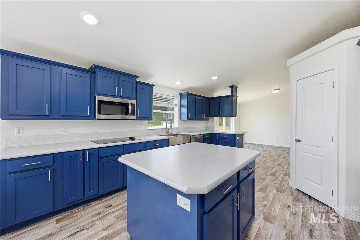 Kitchen with blue cabinets, light countertops, a kitchen island, light wood finished floors, and appliances with stainless steel finishes