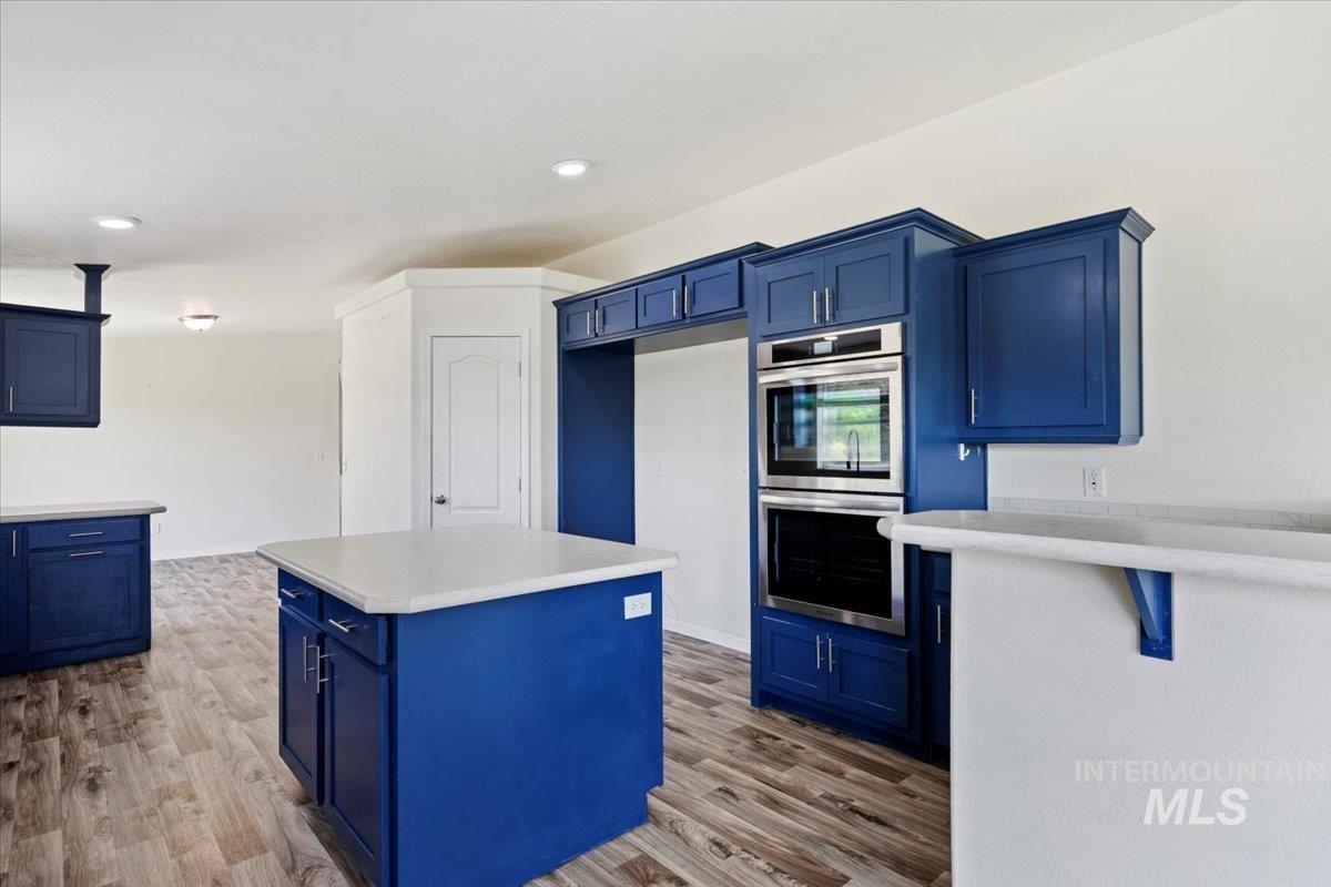 Kitchen with blue cabinetry, a center island, light countertops, double oven, and light wood-style flooring