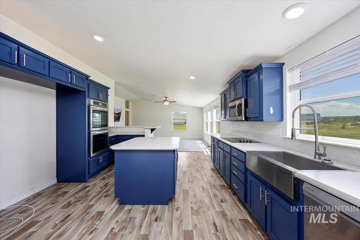 Kitchen with blue cabinetry, appliances with stainless steel finishes, ceiling fan, light wood-type flooring, and recessed lighting