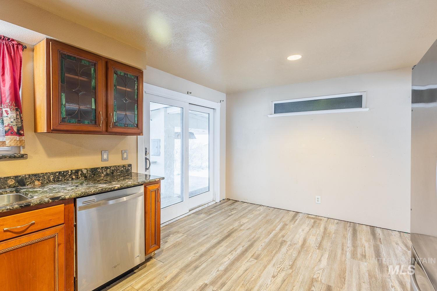 Kitchen with brown cabinetry, stainless steel appliances, dark stone countertops, glass insert cabinets, and light wood-style floors