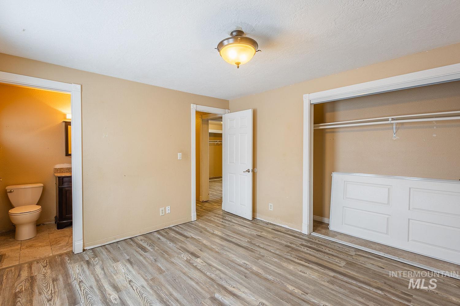 Unfurnished bedroom with light wood-style flooring, a closet, ensuite bath, and a textured ceiling